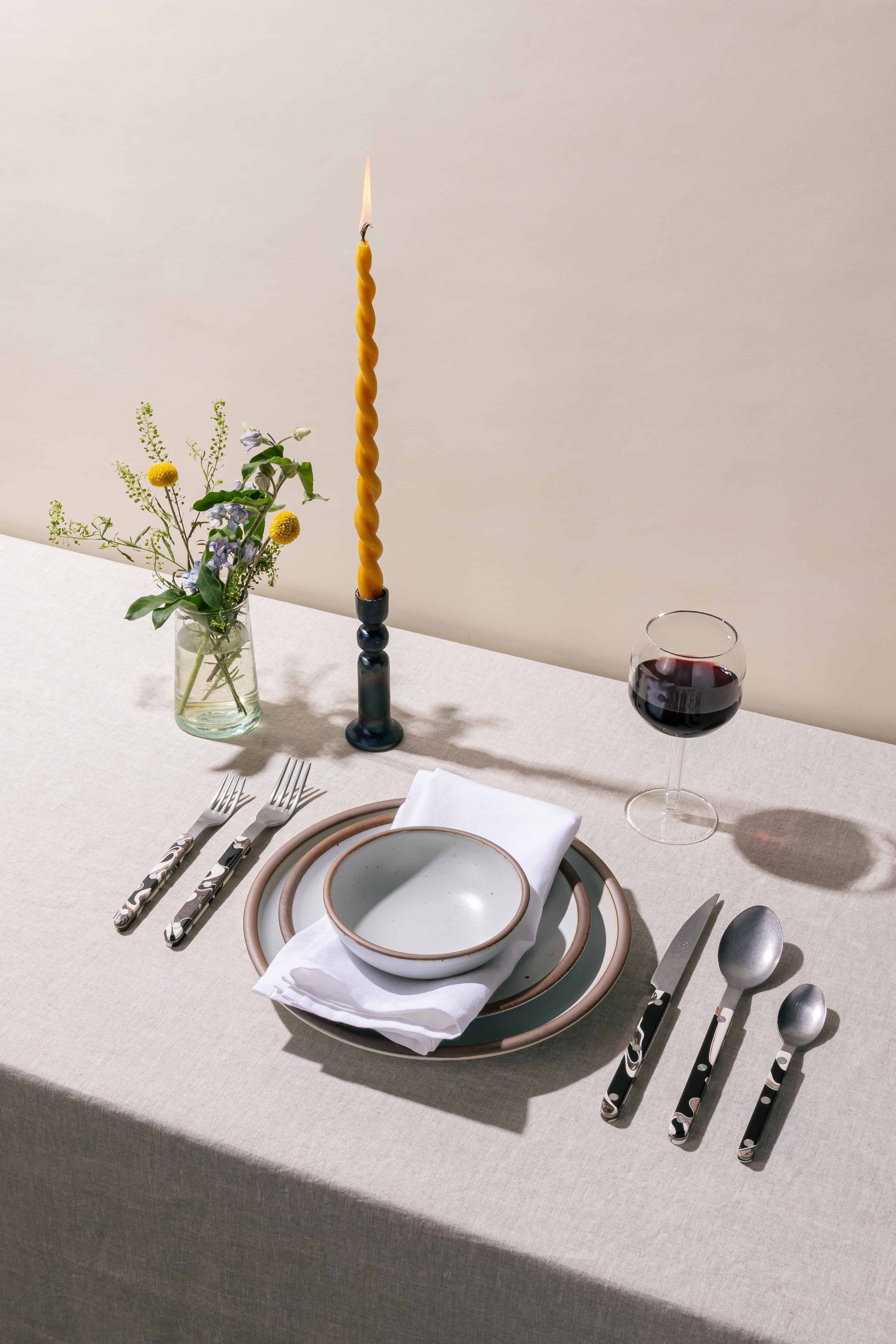 A table setting featuring ceramic plates in a white color, a white napkin napkin, a twisted taper candle, and marble-handled flatware.