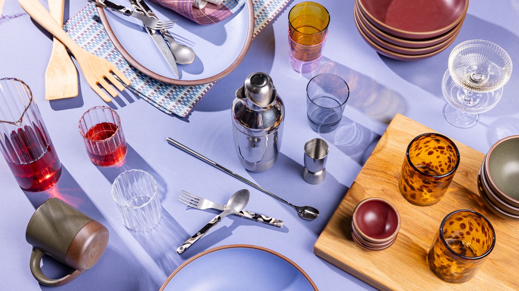 A collection of gifts including a cocktail shaker set, glassware, a mug, a large oval platter, and more against a periwinkle background.