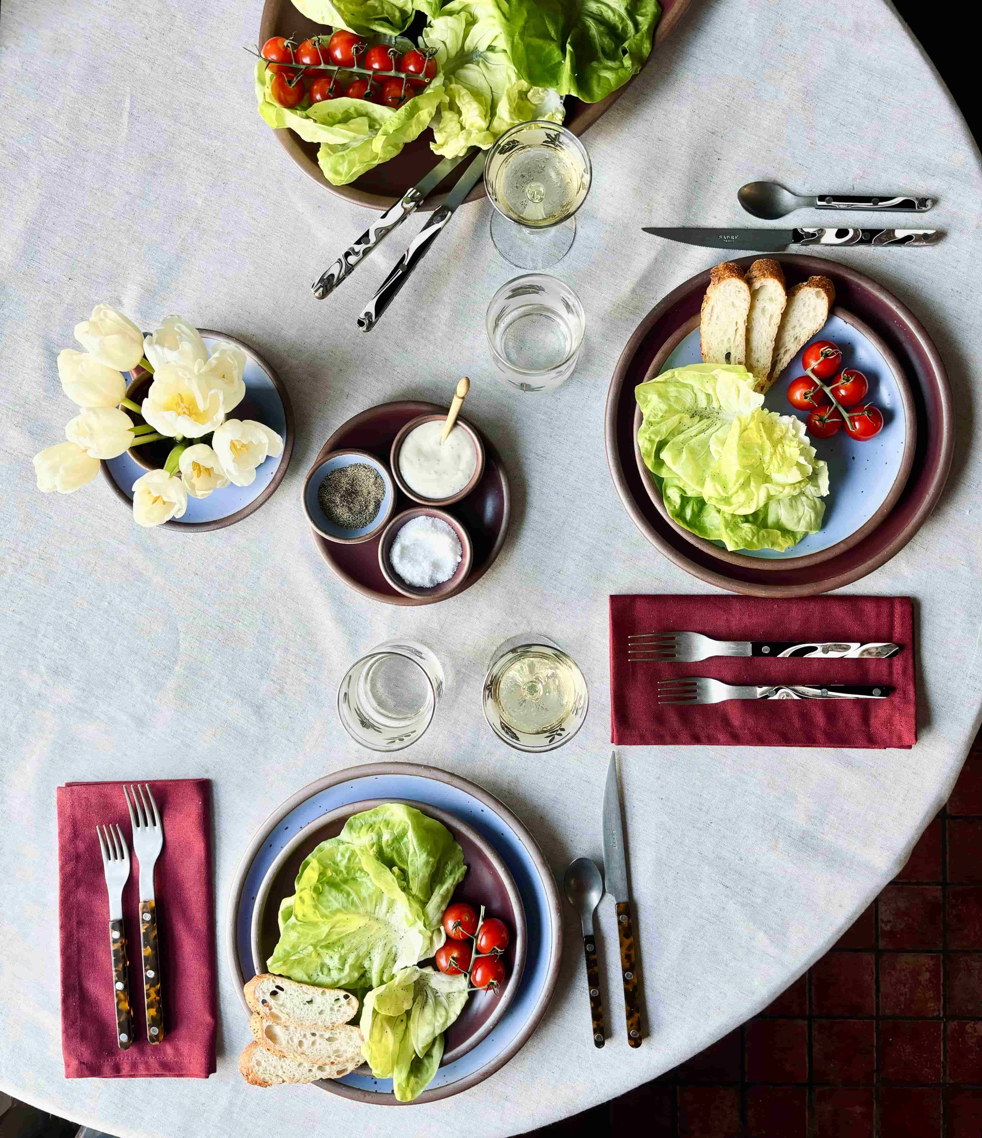 Salads are on artful place settings featuring marbled flatware, periwinkle and plum plates, and plum napkins.