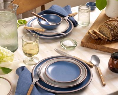 Bright table setting with blue and white stoneware, fresh bread, etched glassware, and wood-handled cutlery on a checkered cloth.