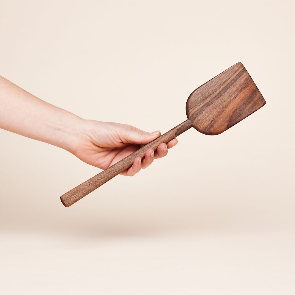 A shovel-shaped dark wood scraper attached to a long handle, held in a hand