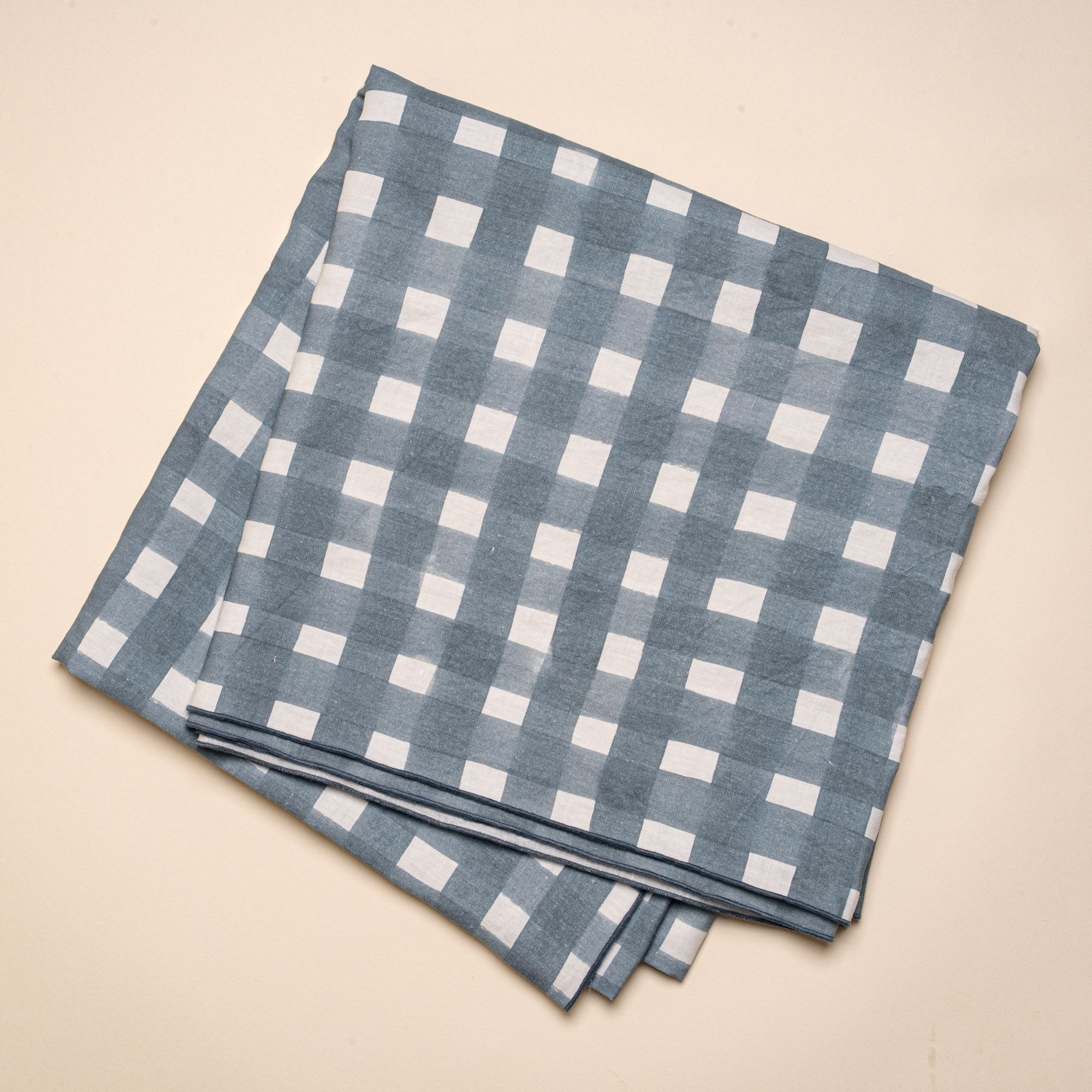 A folded tablecloth featuring a blue-grey crosshatch pattern with navy edges.