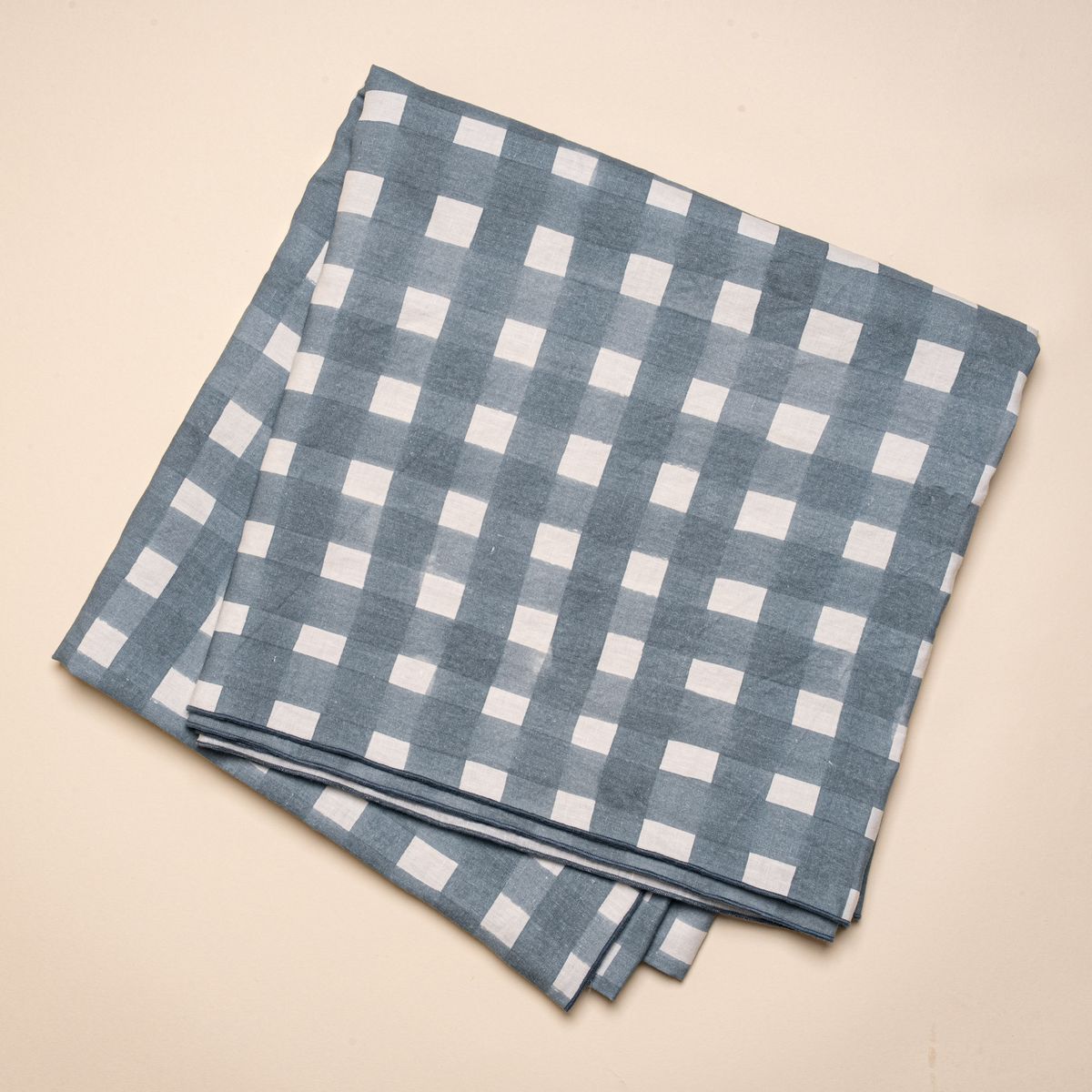 A folded tablecloth featuring a blue-grey crosshatch pattern with navy edges.