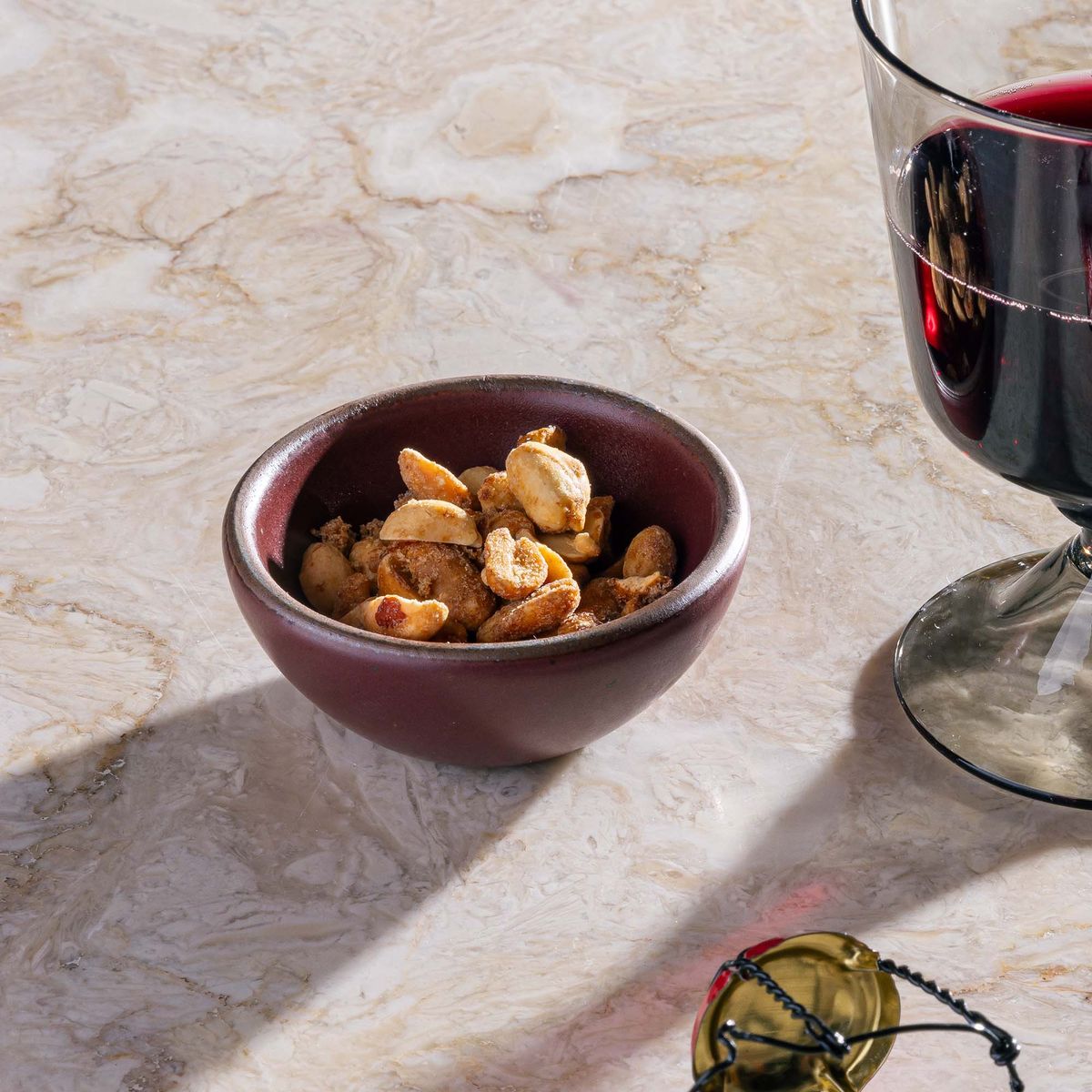 A tiny rounded ceramic bowl in a plum color filled with nuts and sitting by a wine glass