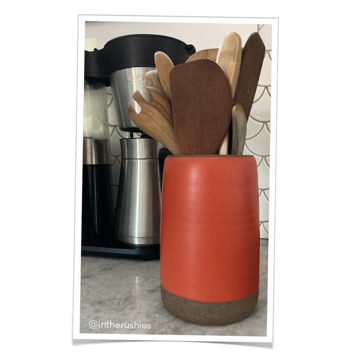A tall utensil holder in a firey red holds wooden kitchen spoons