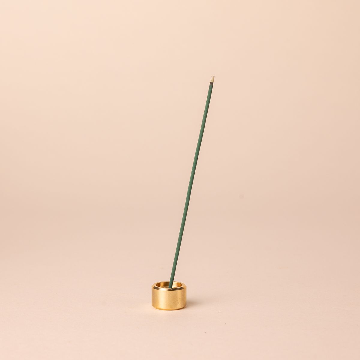 A short small brass cylinder incense holder with a teal incense stick sitting on top.