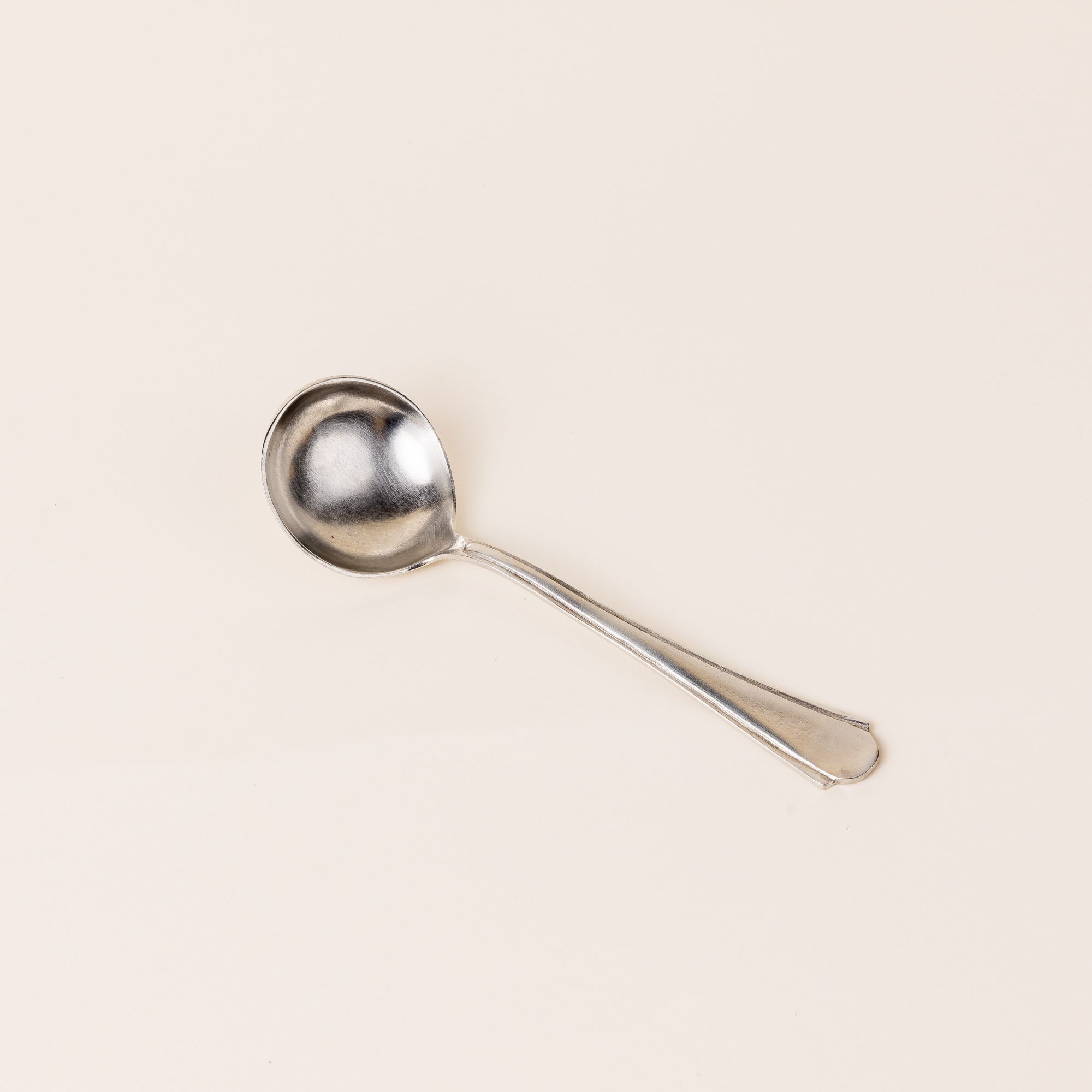 A silver spoon with a skinny handle that gets a little wider and round on the end. The bowl of a spoon is circular.