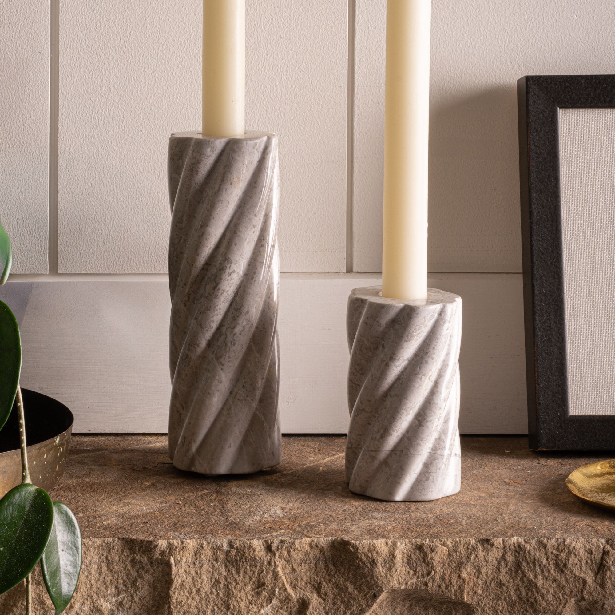 Two gray marble candle holders with spiral grooves, each holding a cream taper candle on a stone mantel.