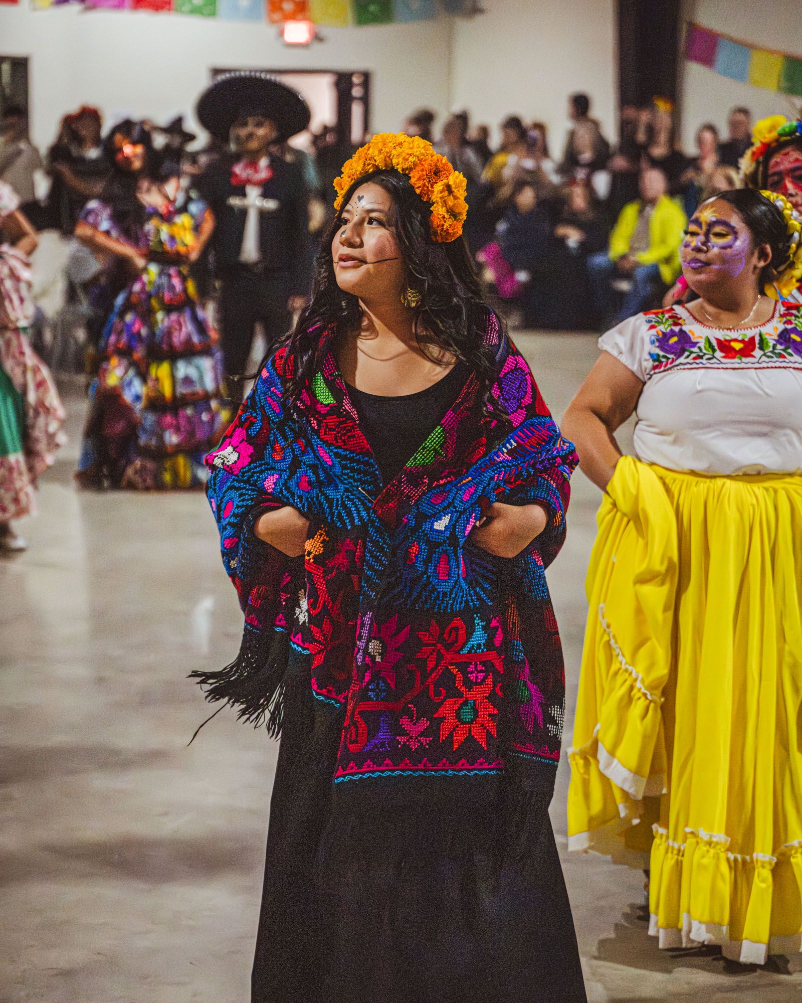 Women wearing face paint and floral headdresses dancing at an indoor festival