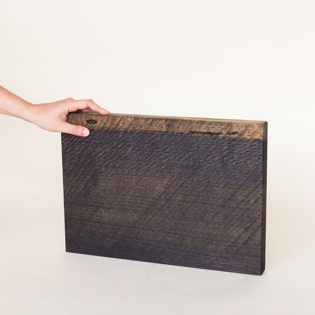 A rectangle of wood that has been finished in an ebonized stain is held by a hand