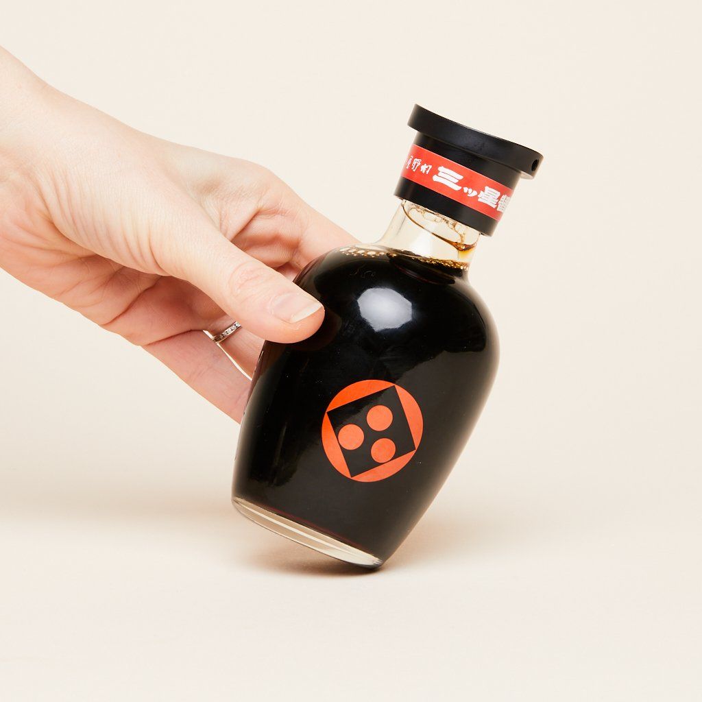 A hand tilts a full, capped bottle of soy sauce