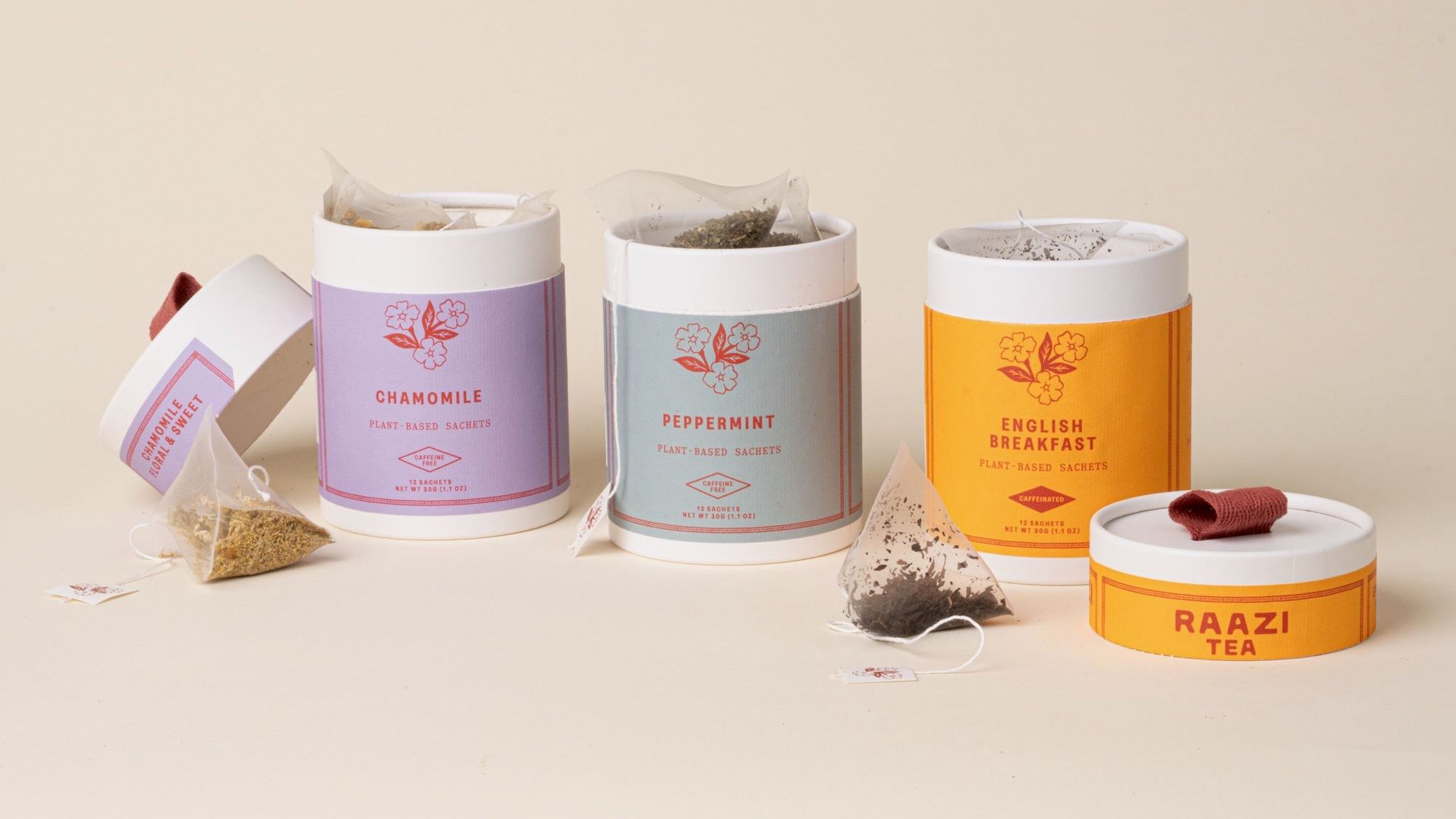 Three open RAAZI Tea tins (chamomile, peppermint, English breakfast) with loose sachets and lids on a neutral background.