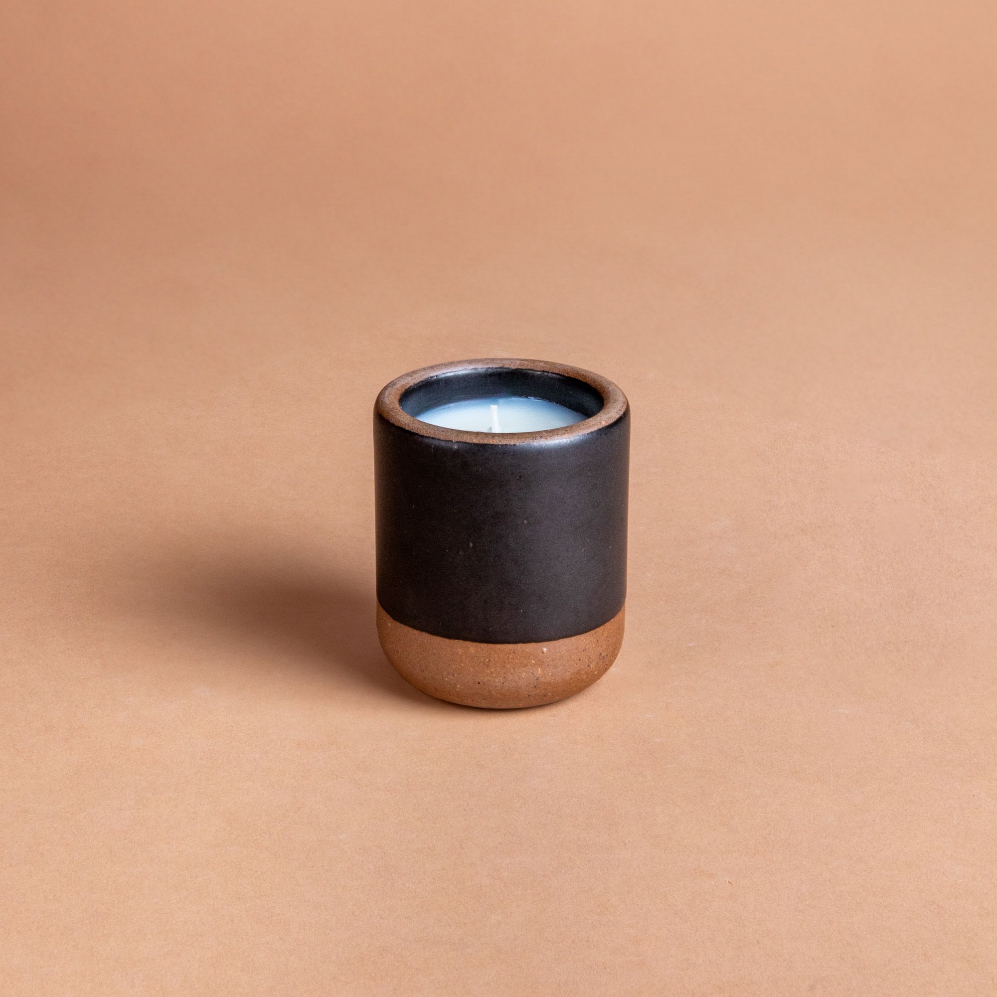 Small ceramic vessel in dark charcoal color with candle inside.