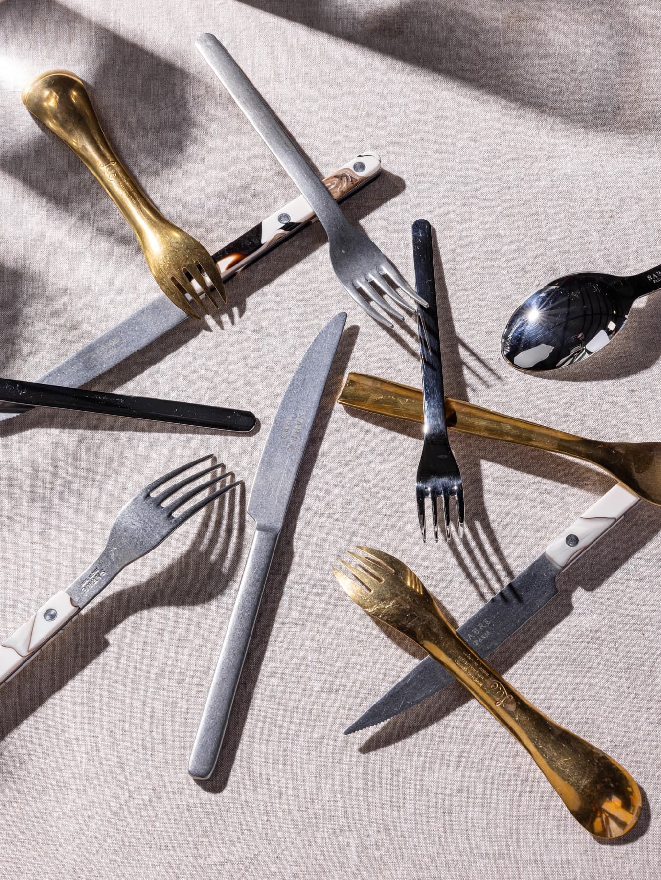 Various styles of forks, knives, and spoons artfully arranged stacked in a chaotic manner.