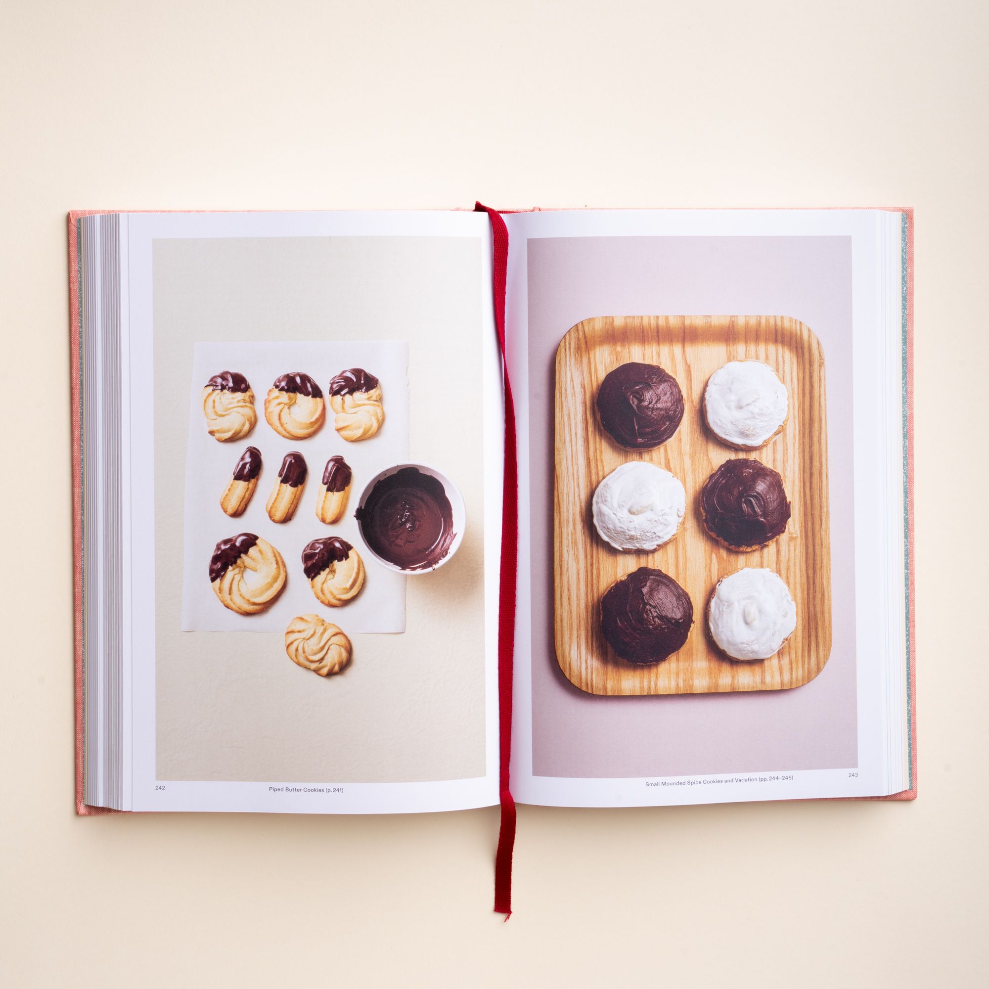 Open cookbook showing butter cookies dipped in chocolate and a wooden tray with six black-and-white cookies.