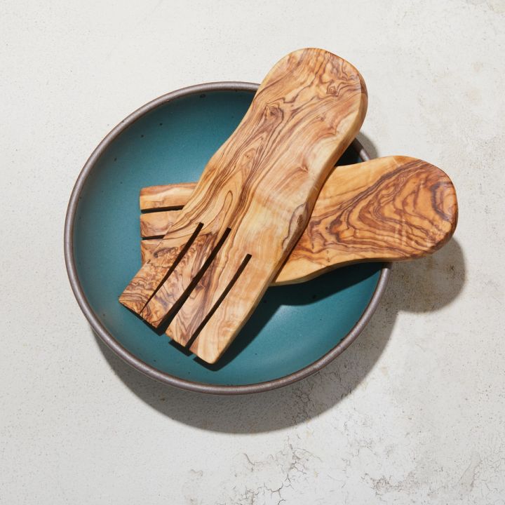 A pair of olivewood serving utensils rest in a large, shallow bowl