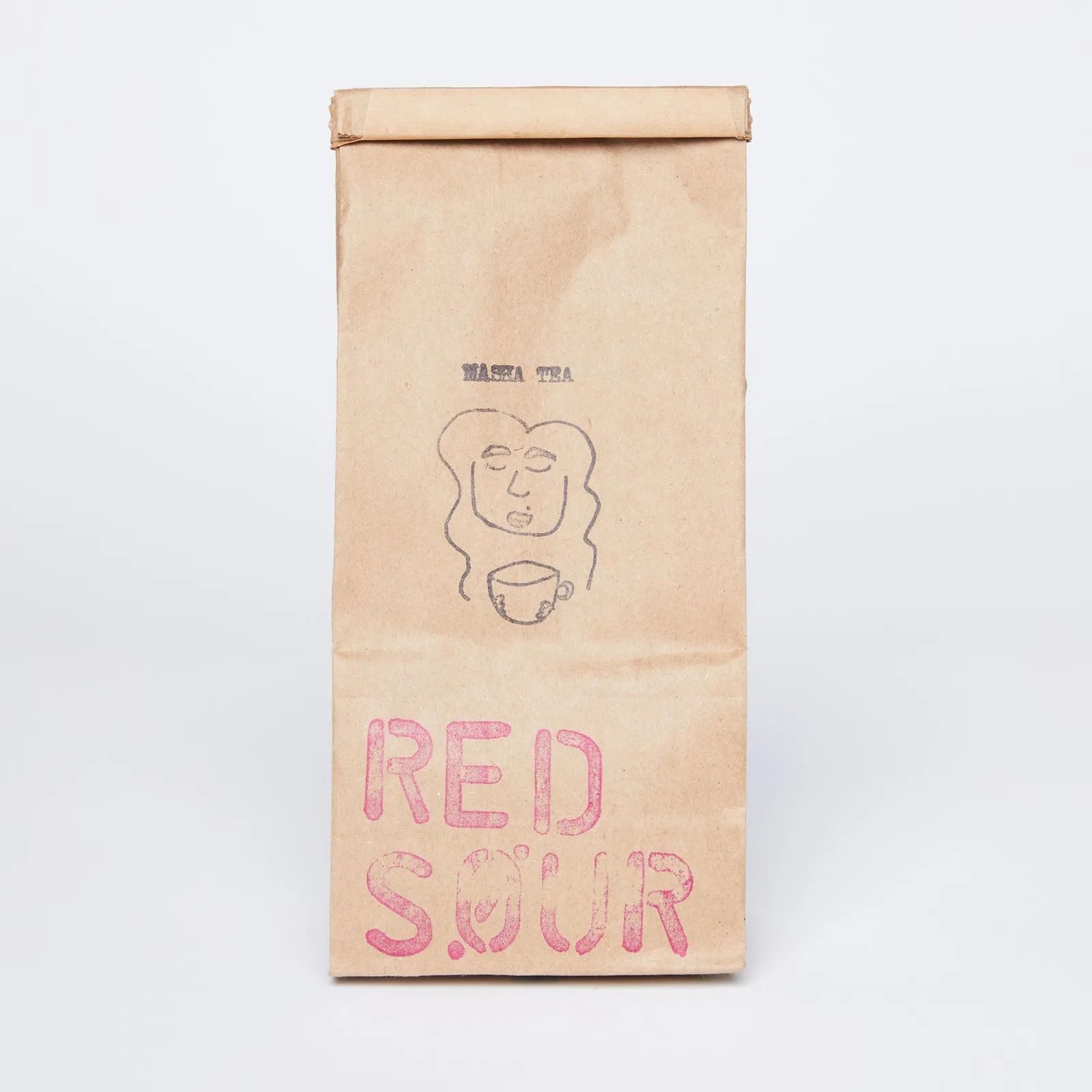 A tan bag of tea with a funky face drawn on it and the words "Red Sour" stamped on it