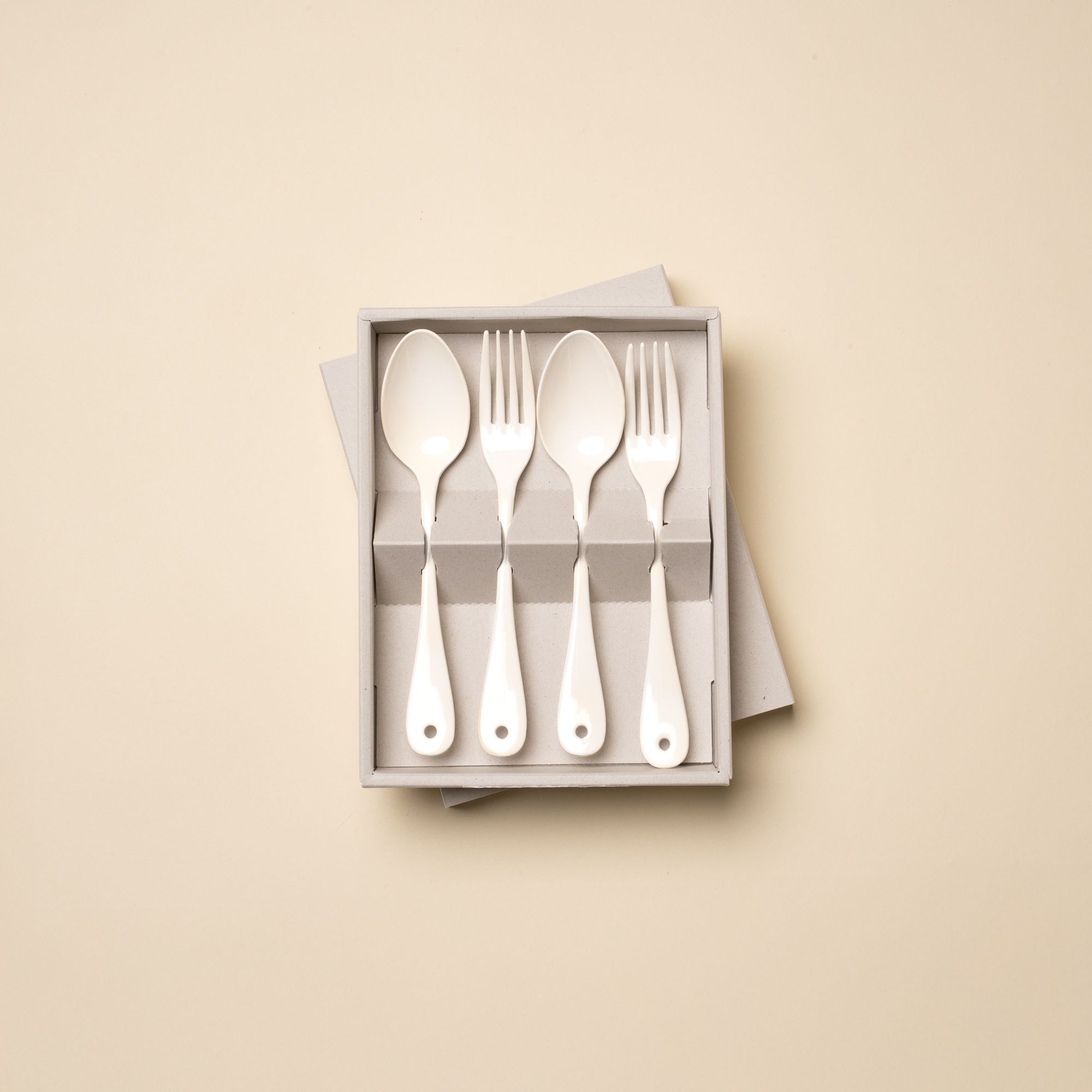 2 dinner forks and 2 dinner spoons made of white enamel lined in a row sitting in an open packaging box.