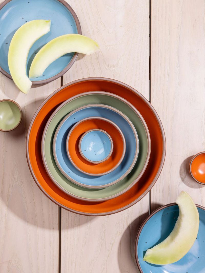 An overhead view of a nesting bowl set featuring 5 bowls - the largest being a kitchen mixing bowl, and the smallest being a tiny bowl for spices. Colors range from bold orange, calming sage green, and a robin's egg blue.