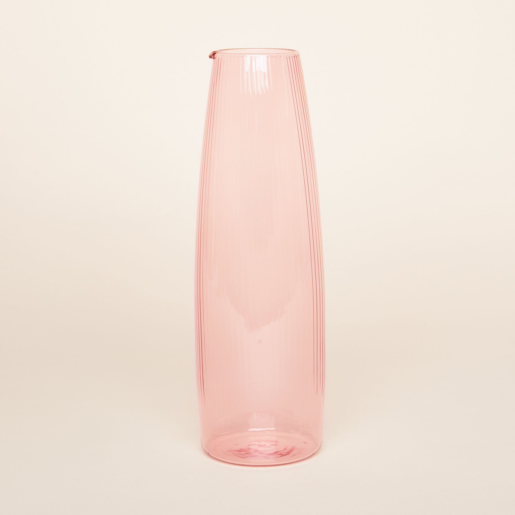 A pitcher that is tall and pale glass with vertical grooves and has a spout at the rim. Comes in three colors: pale yellow, a zesty but translucent green, and a festive but soft pink.