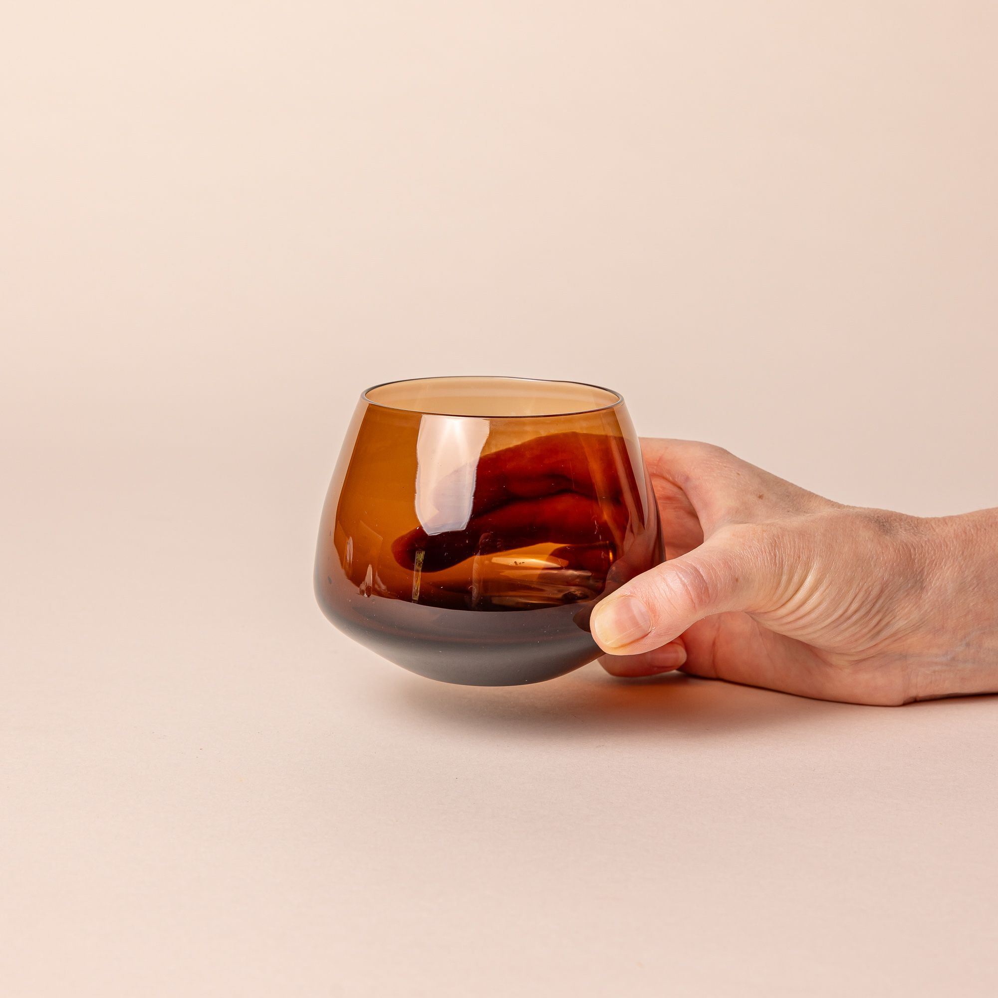 A hand holding a brown glass whiskey snifter with a rounded base