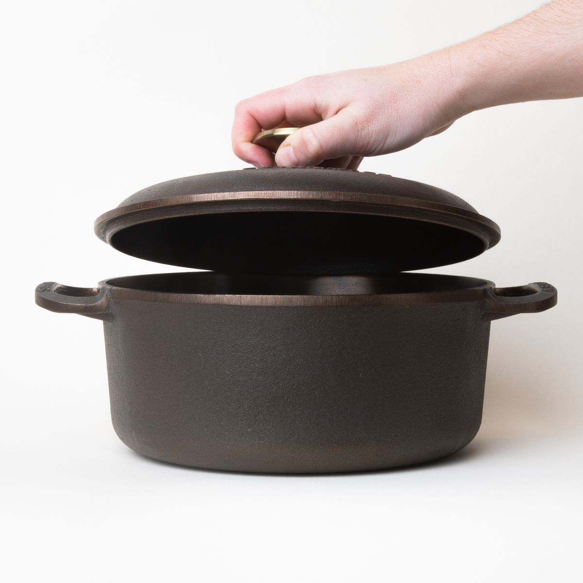 Hand holding the cast iron lid over a cast iron dutch oven with a handle on each side