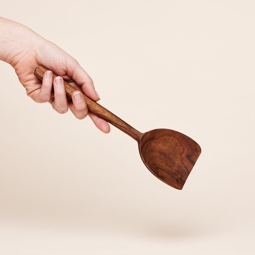 A hand holds a brown scoop made of walnut wood