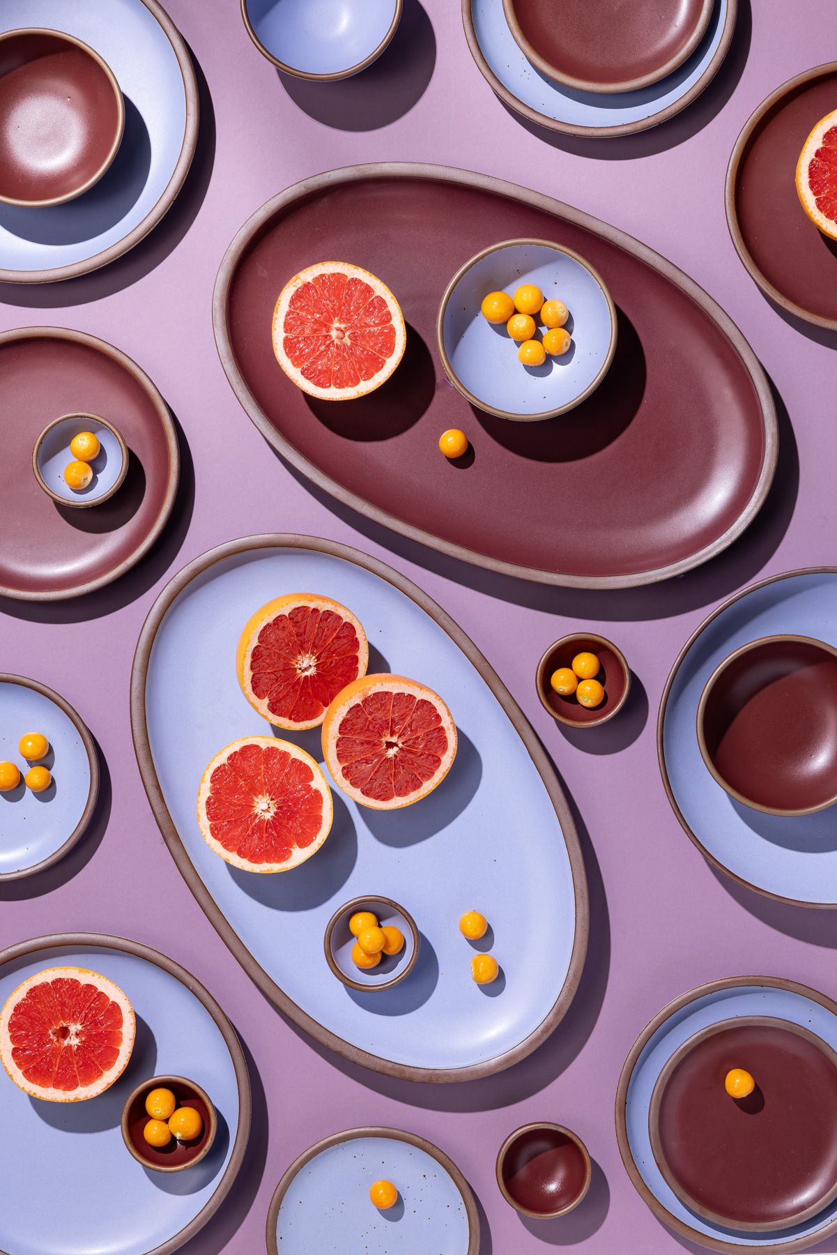 An artful layout of ceramic dishes in periwinkle and plum including oval platters with grapefruit.