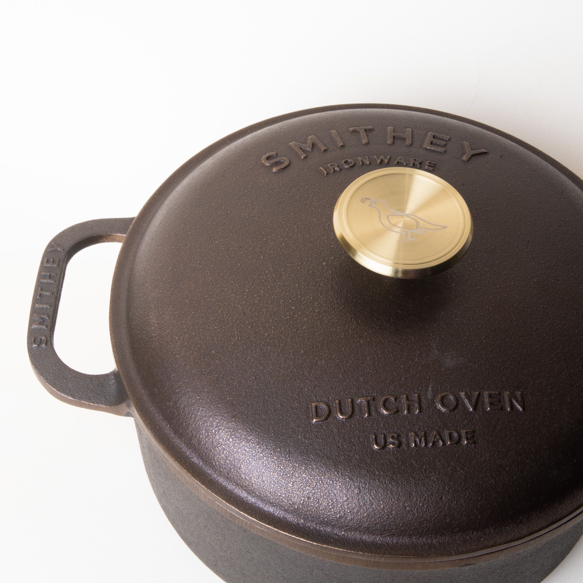 A cast iron lid with a gold metal knob in the center and surrounding it reads "Smithey Dutch Oven"