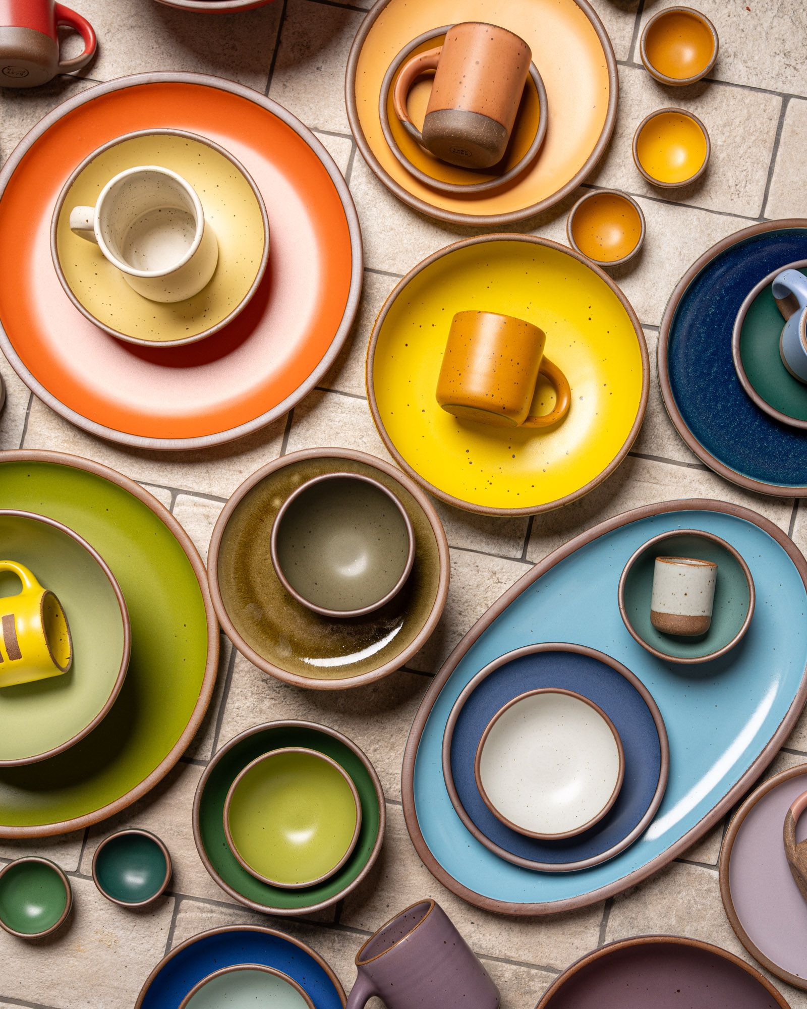 Ceramic dinnerware of plates, platters, bowls, mugs and cups are all artfully arranged close together all in different colors of the rainbow.