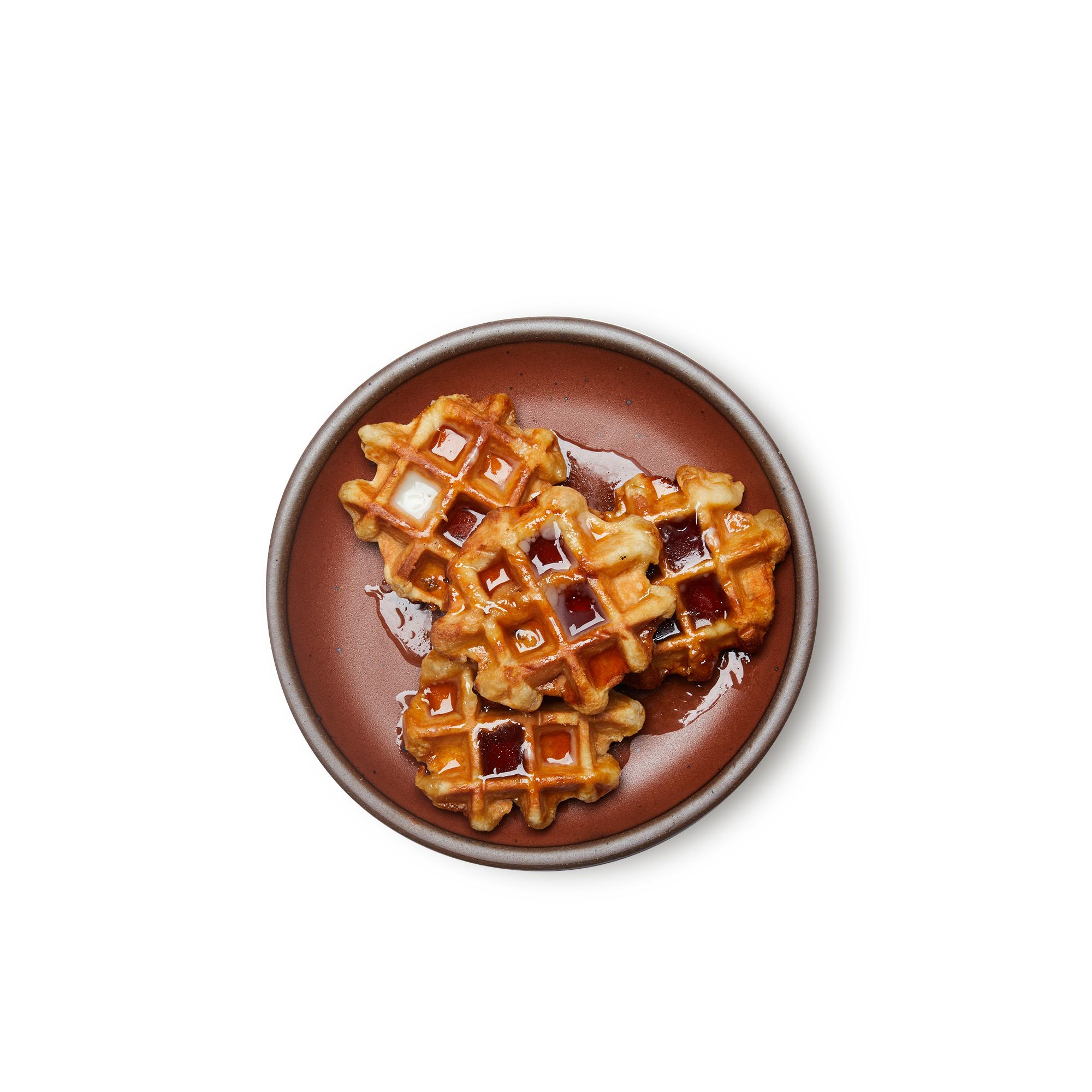 A medium sized ceramic plate in a cool burnt terracotta color featuring iron speckles and an unglazed rim, with waffles and syrup
