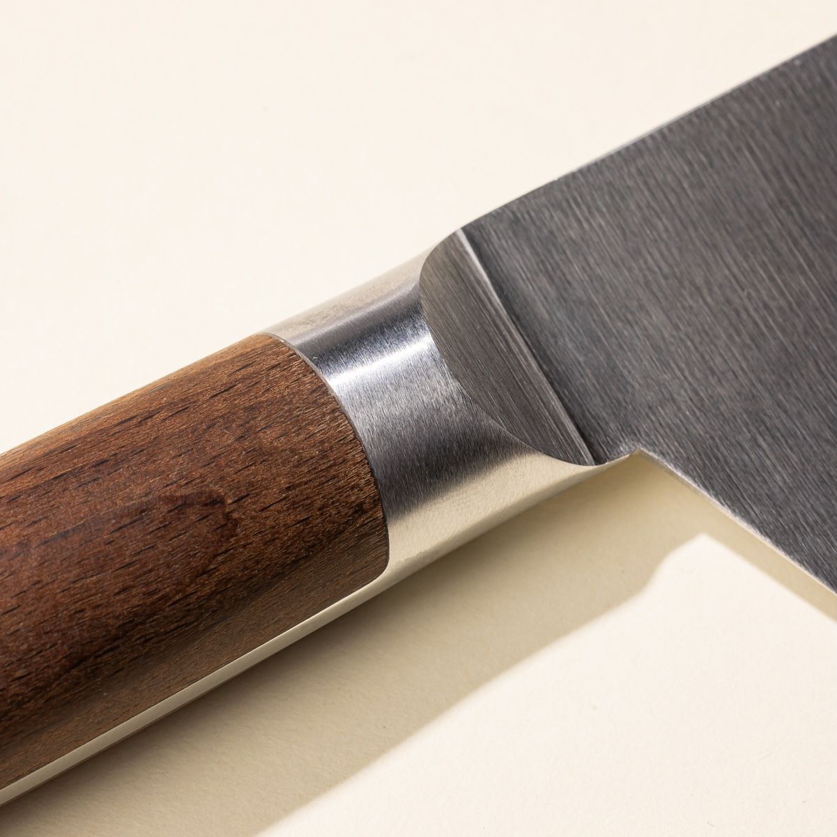 A close up of where the wooden handle meets the steel blade of a chef's knife