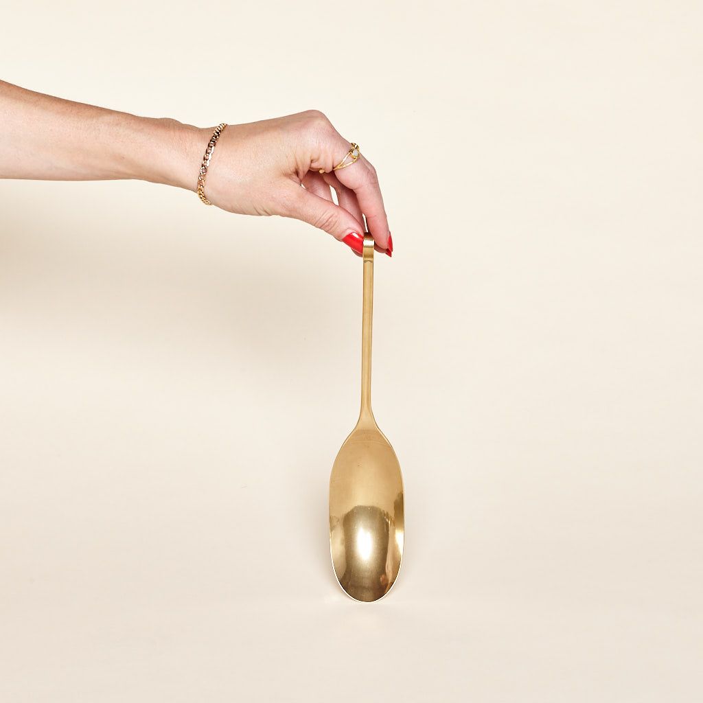 Fingers grasp the end of a long brass spoon