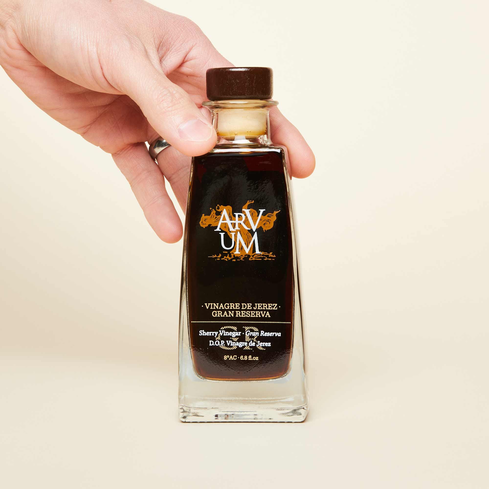 A hand touches a bottle of sherry vinegar, which is dark brown.
