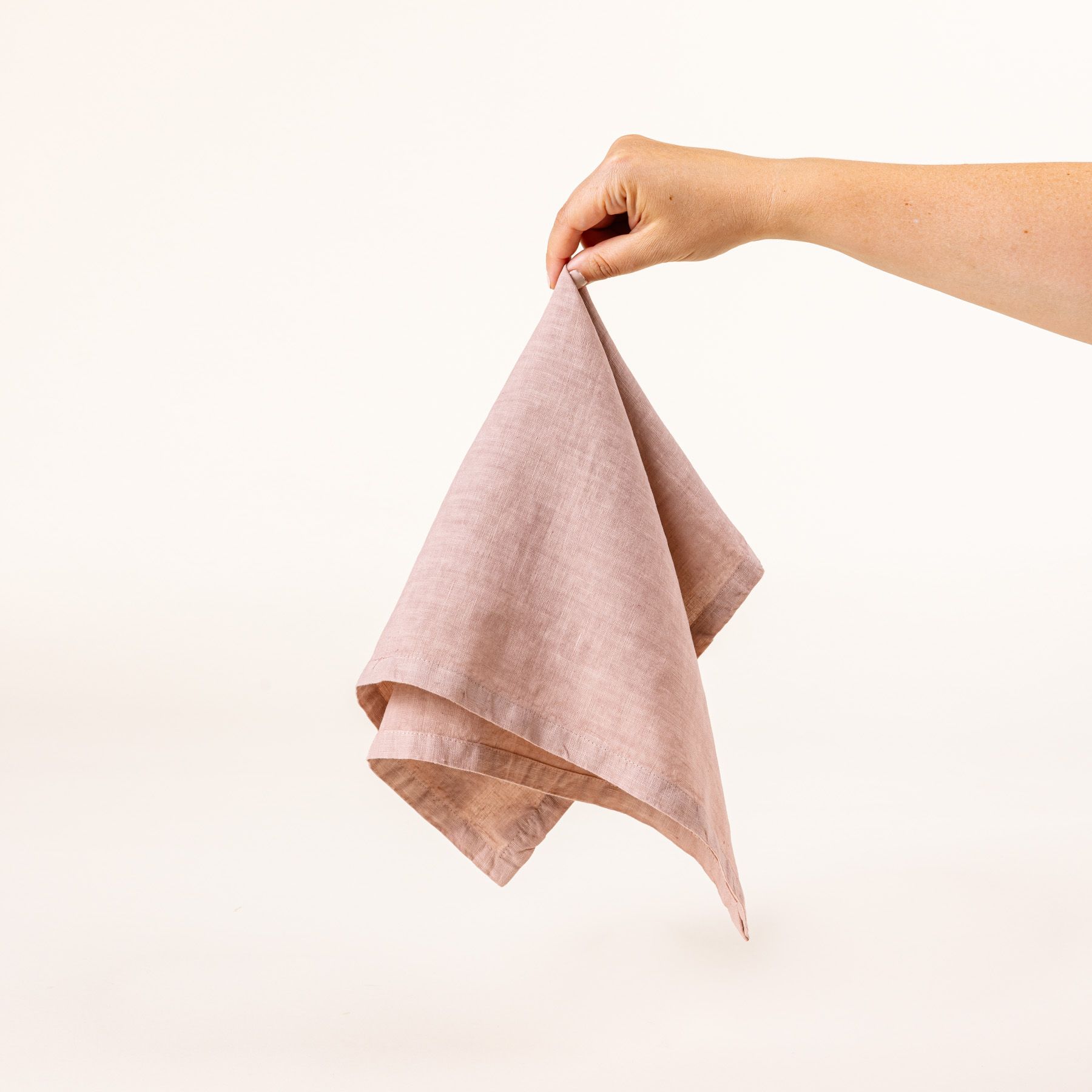 A hand holds a linen napkins in a soft pink color