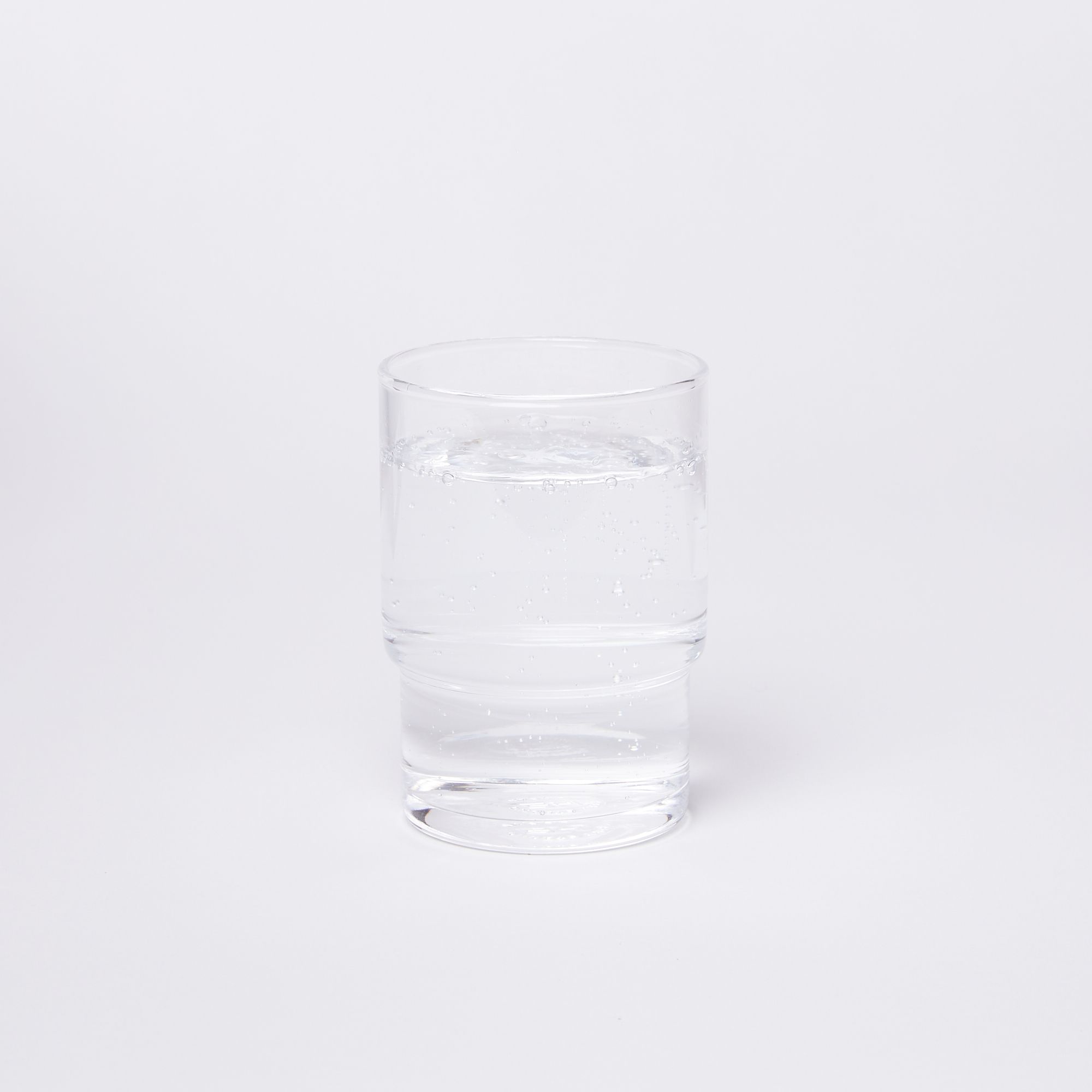 Clear cylindrical glass with a wider top half with a narrower bottom half, full of water