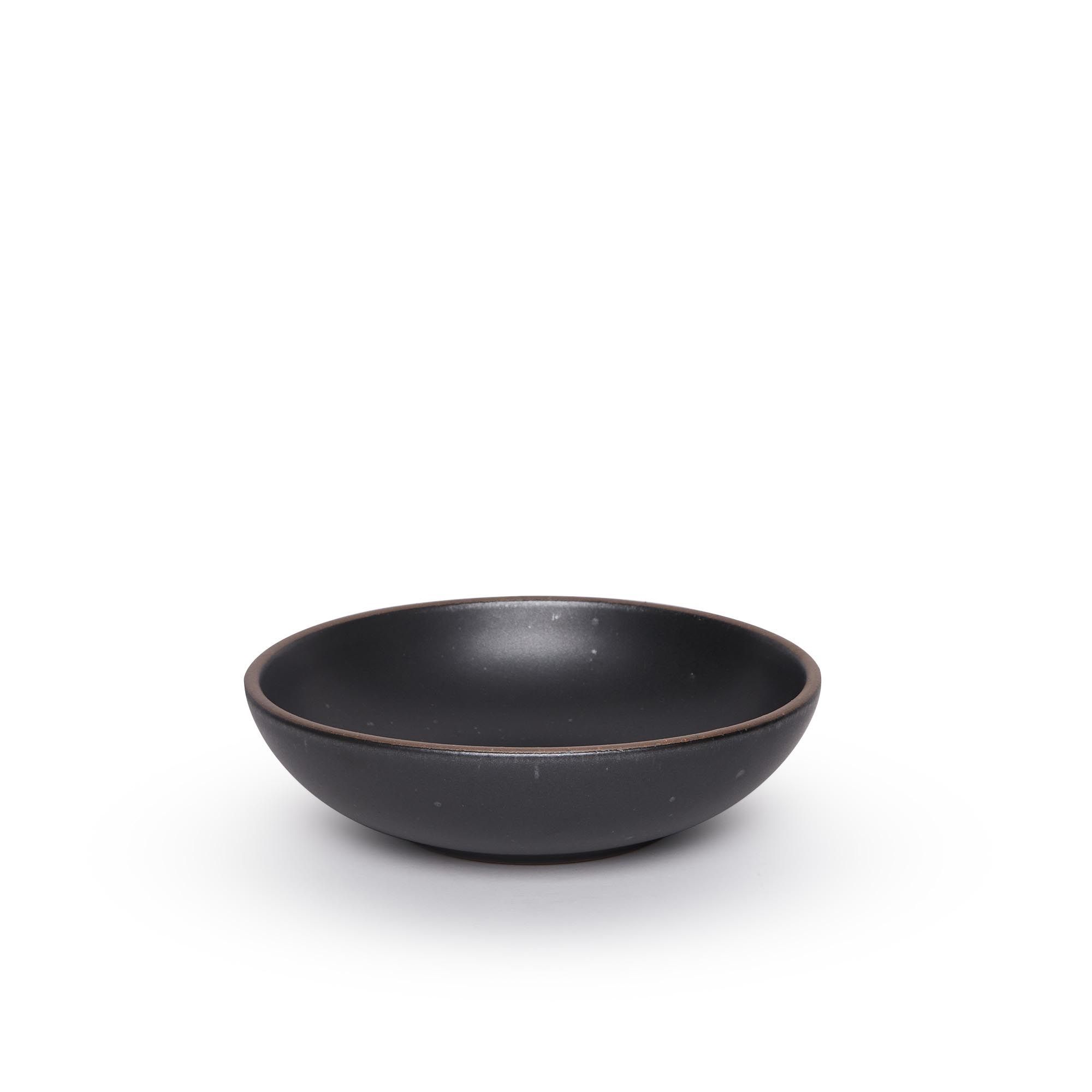 A dinner-sized shallow ceramic bowl in a graphite black color featuring iron speckles and an unglazed rim