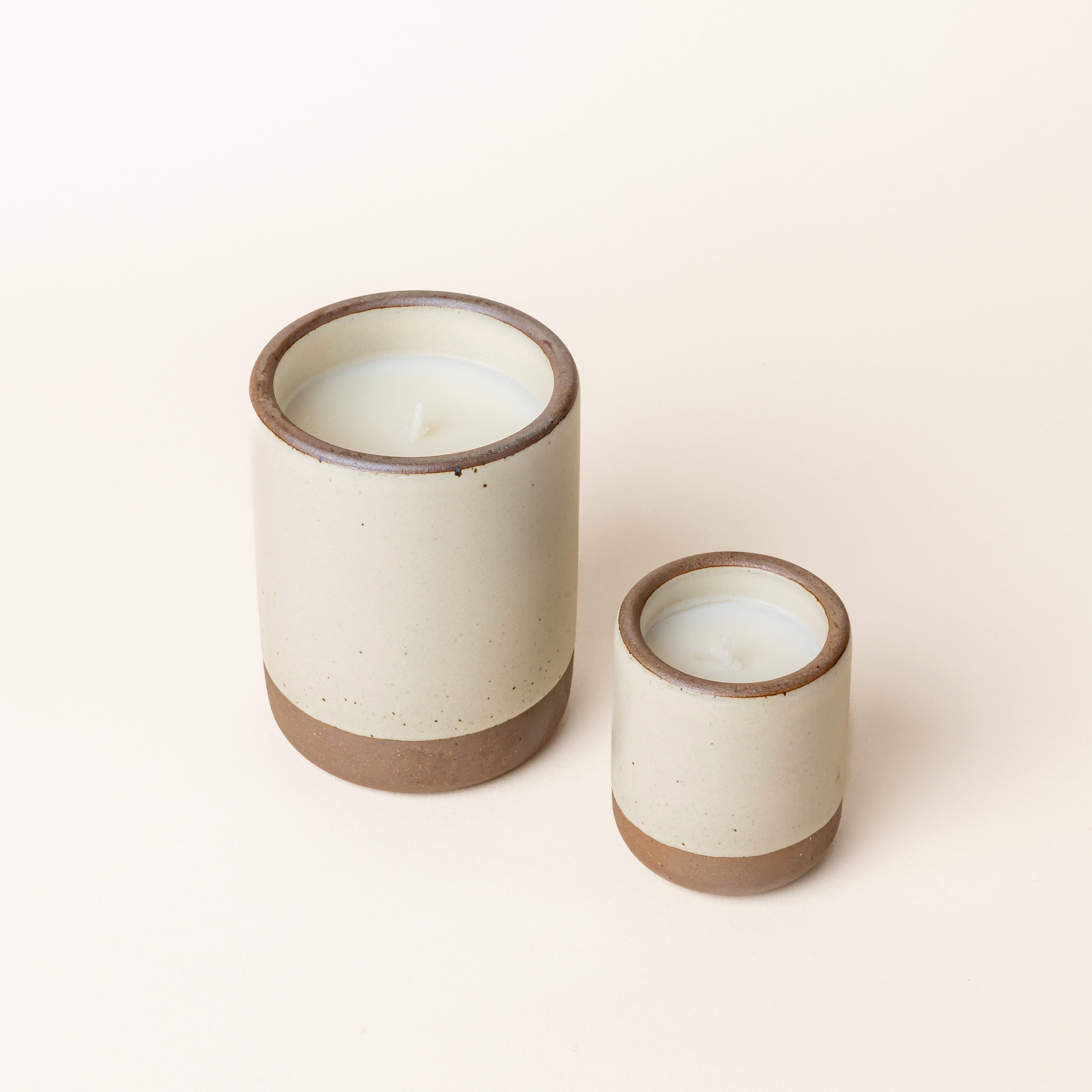 A large and small ceramic vessels in a warm, tan-toned, off-white color with candle inside each.