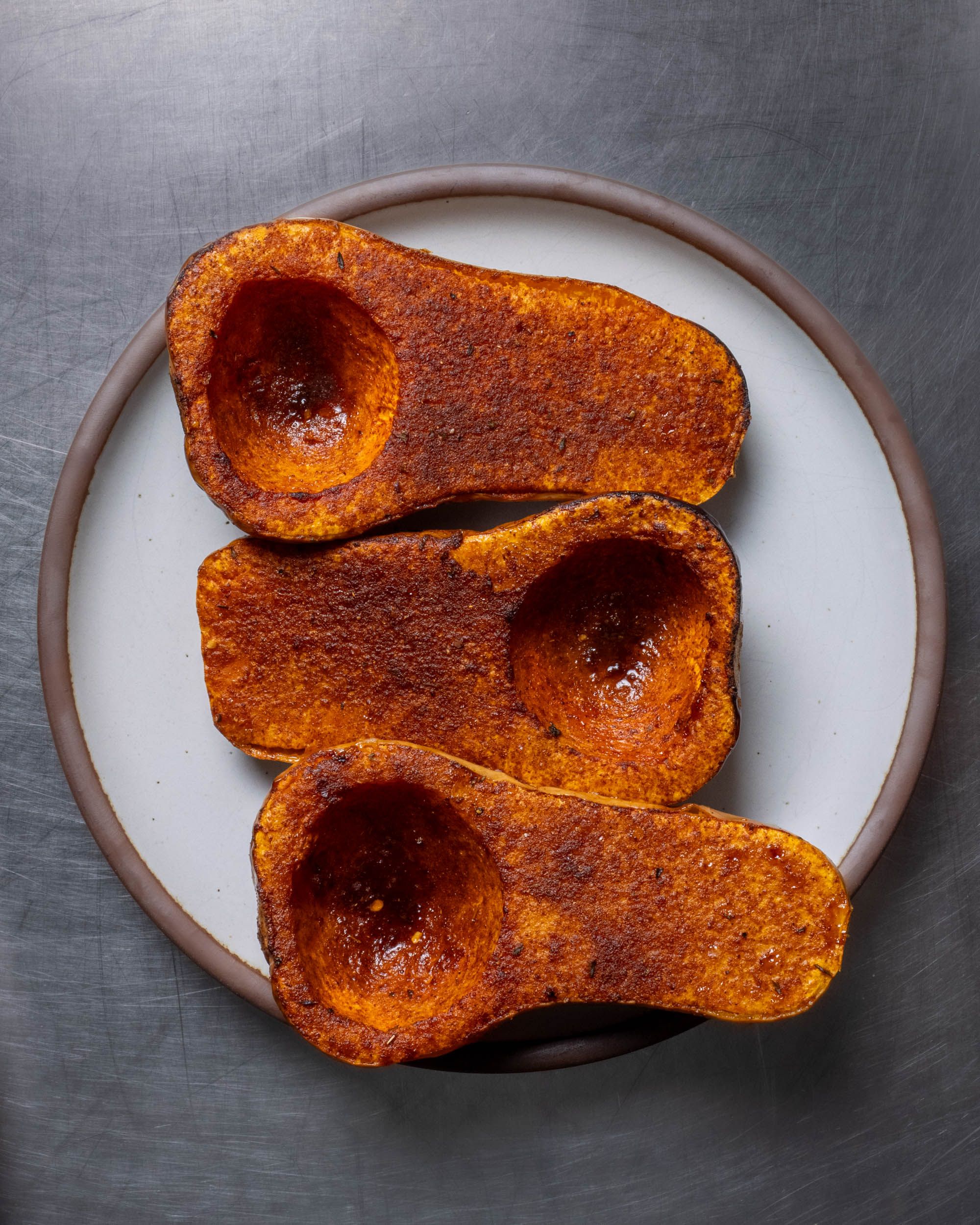 Three sliced roasted butternut squash halves with seasoning on top sitting on a white plate.