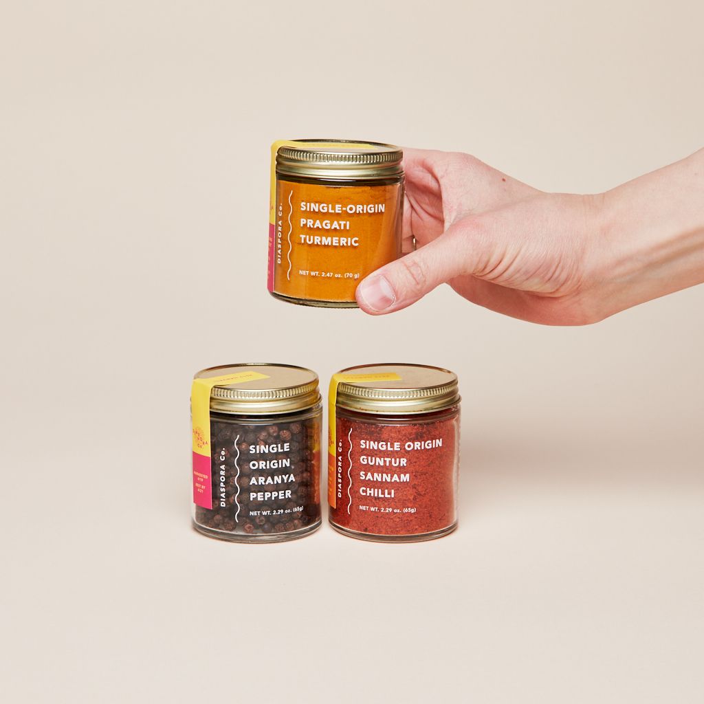A trio of jars filled with spices, a hand holding the one filled with turmeric