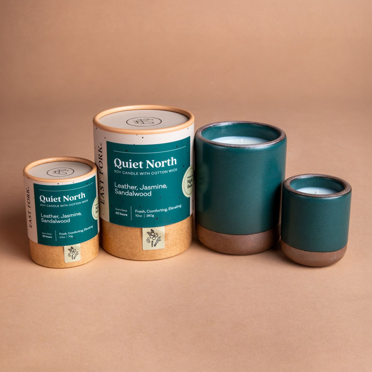 Small and large ceramic vessel next to each other in a dark teal color with candles inside each. Cardboard tube packaging is on the left with branding stickers that say "Quiet North".
