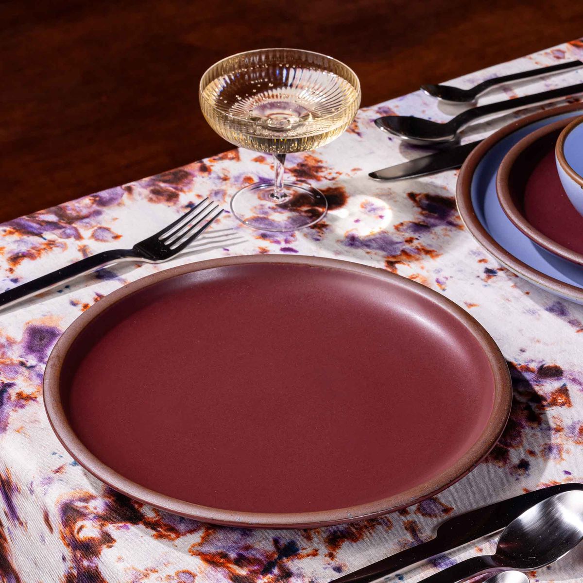 A table setting featuring marbled textiles, a coupe glass, and a dinner plates in plum