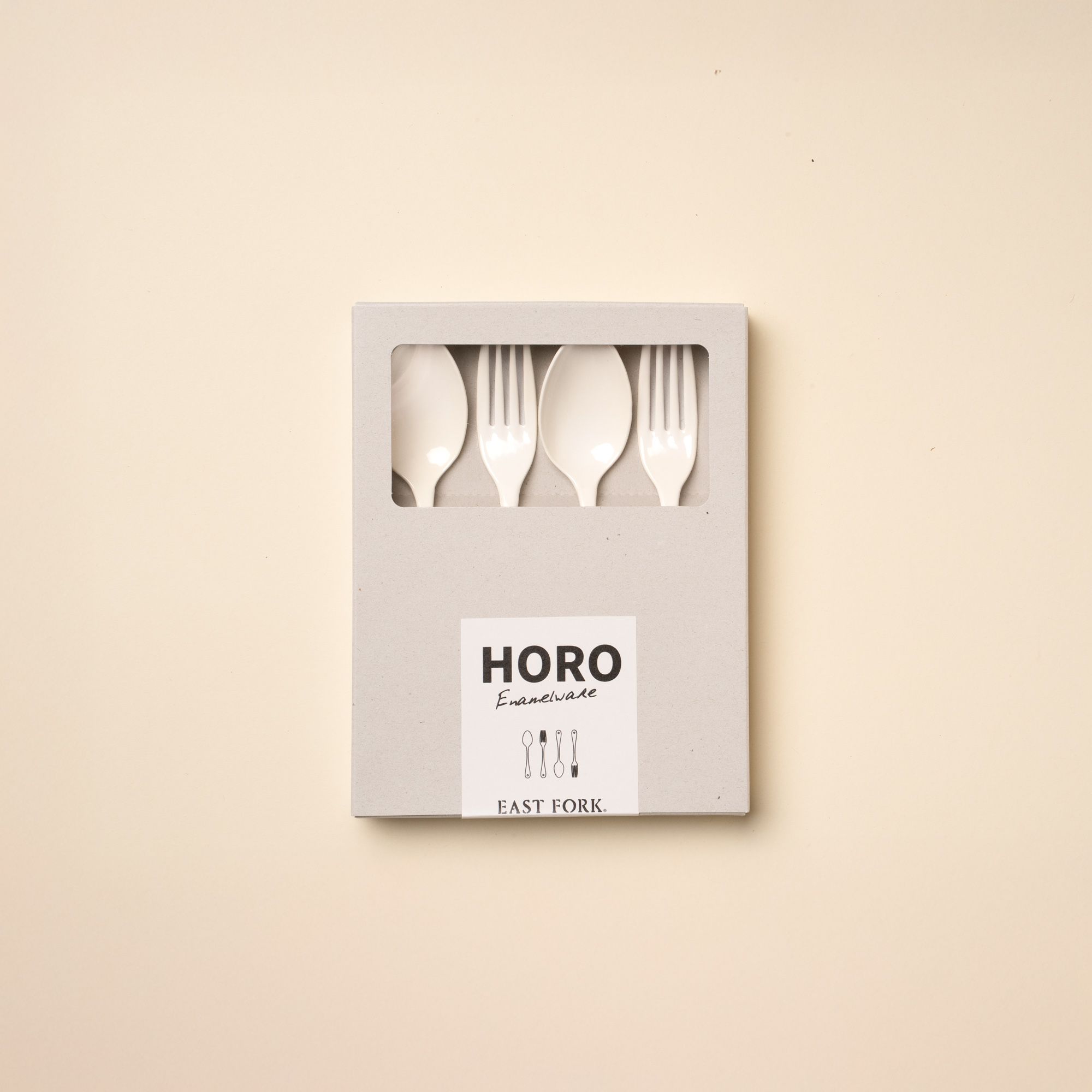 2 dinner forks and 2 dinner spoons made of white enamel lined in a row sitting in a closed packaging box.