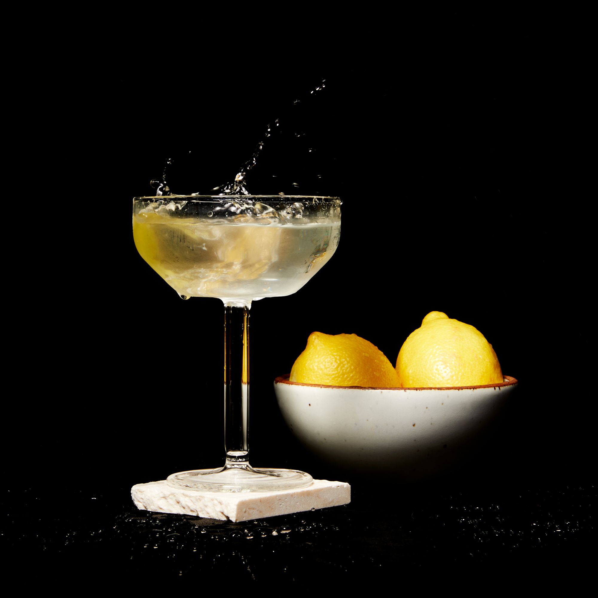 A clear martini glass filled with a martini with a bowl of lemons nearby