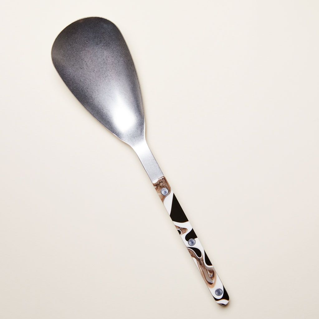 A serving spoon with an elongated silver-colored bowl with a brown and white handle