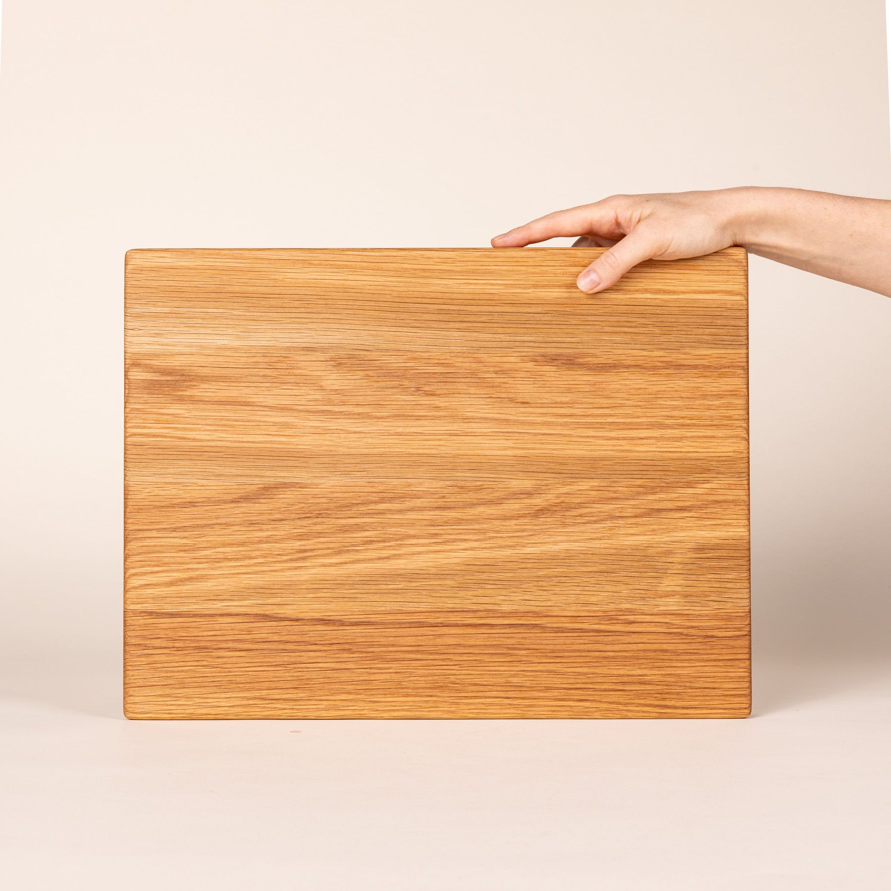 A hand props up a medium rectangular white oak cutting board on its side