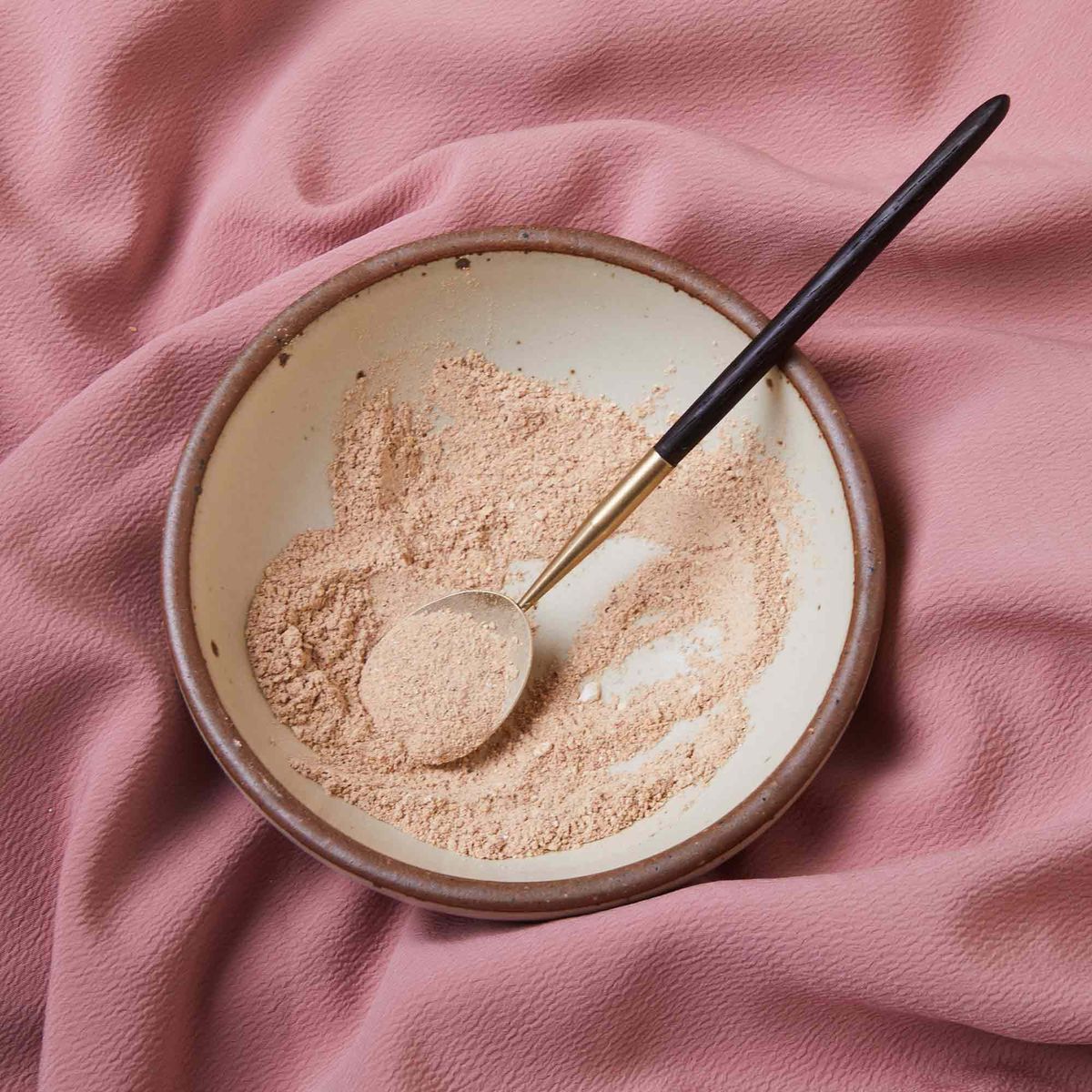 A long-handled brass spoon sits in a pile of pink flour-like powder in an East Fork bowl