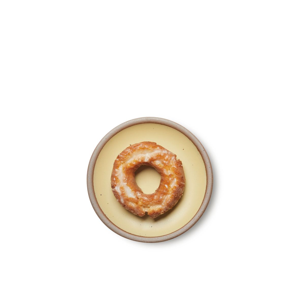 A glazed cake donut on a dessert sized ceramic plate in a light butter yellow color featuring iron speckles and an unglazed rim