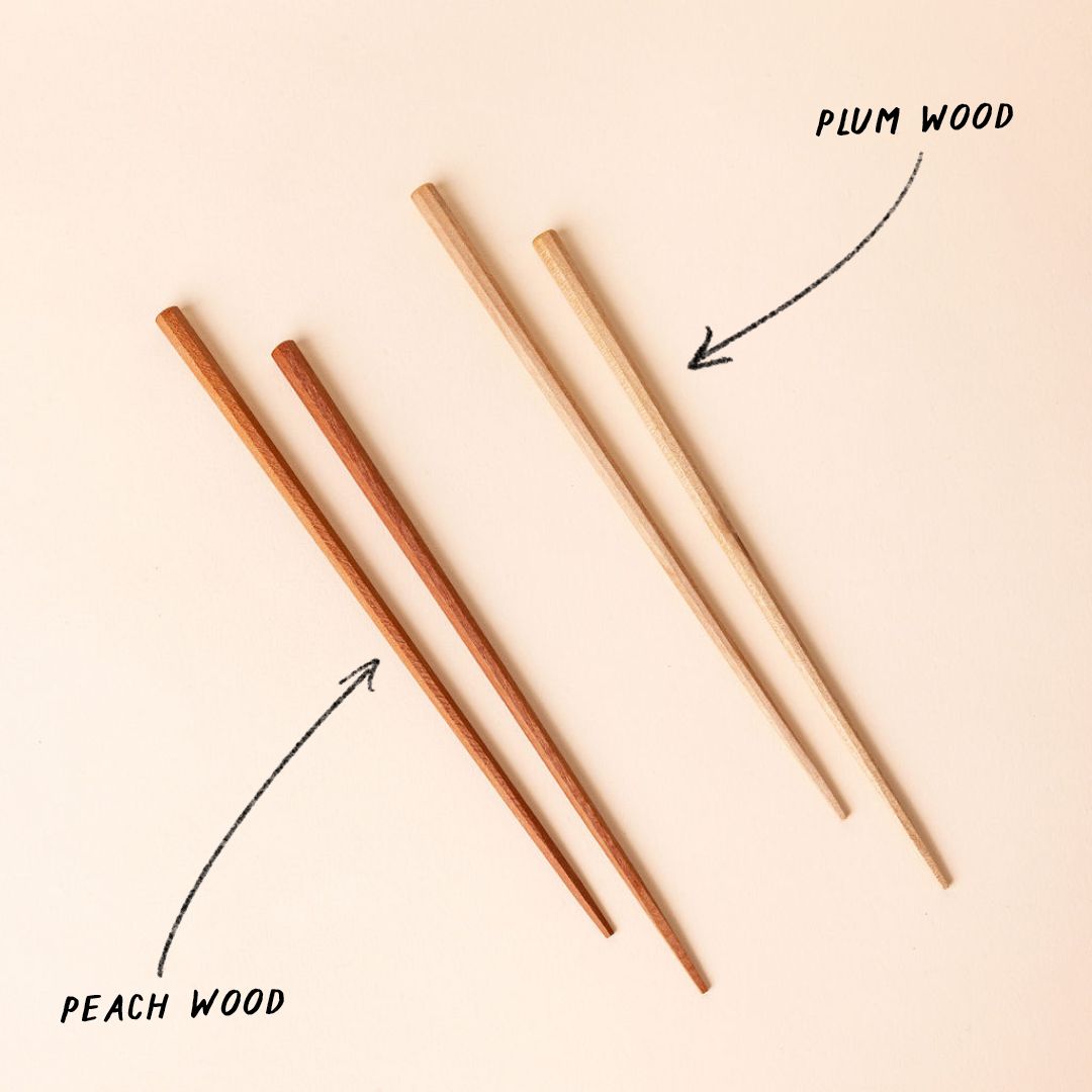 Two pairs of wood chopsticks arranged side by side, with a drawn graphic with an arrow pointing to each pair. The right pair has a plum wood color, the left pair has a peach wood color.