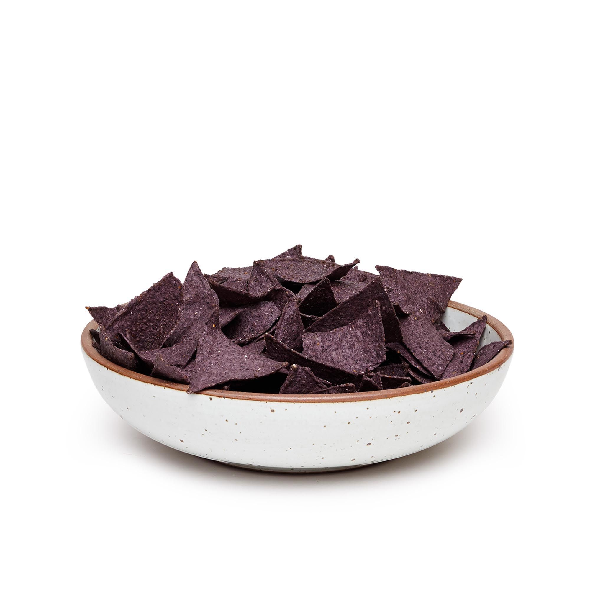 A large shallow serving ceramic bowl in a cool white color featuring iron speckles and an unglazed rim, filled with tortilla chips